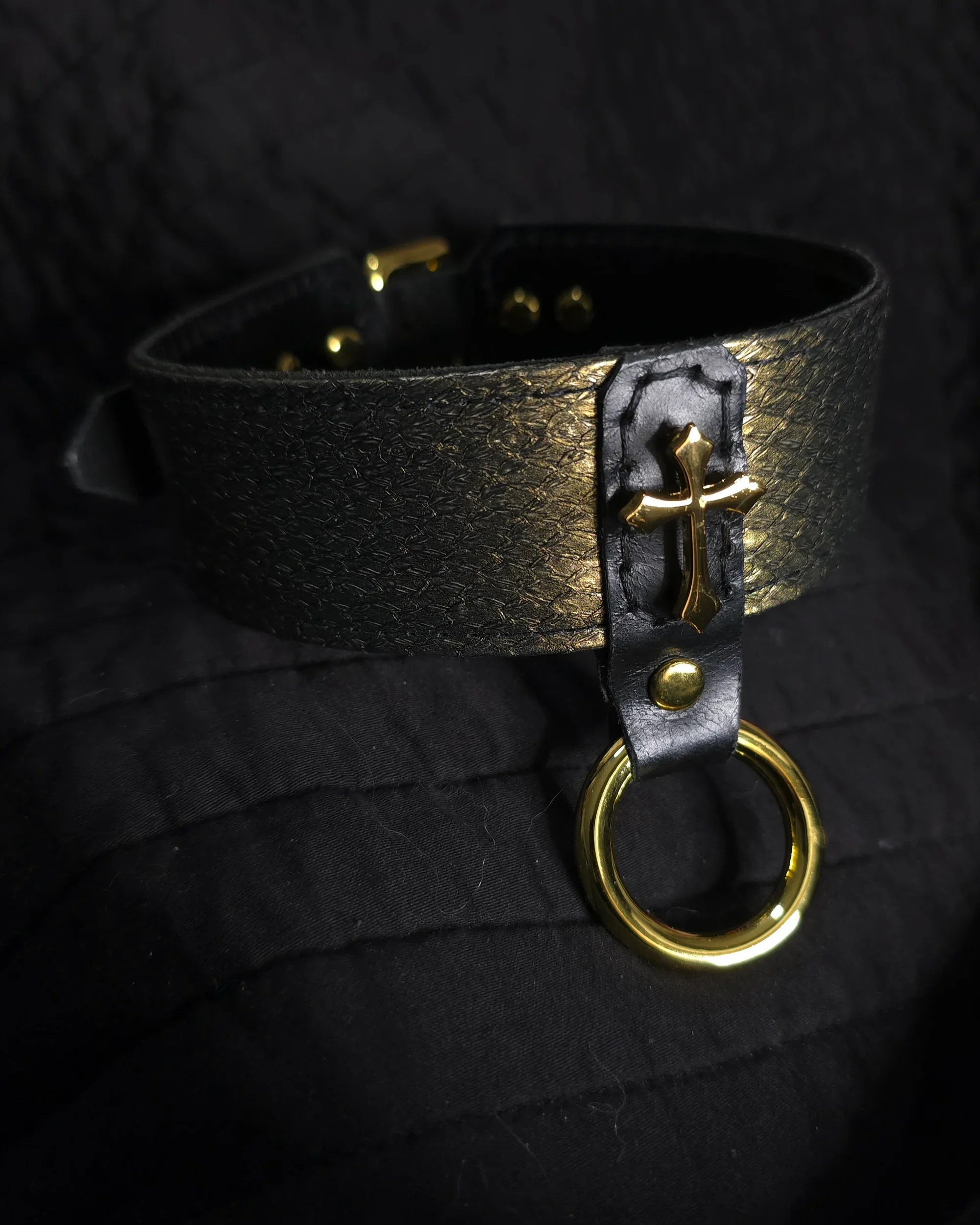 Black leather choker with gold cross and ring on a black background