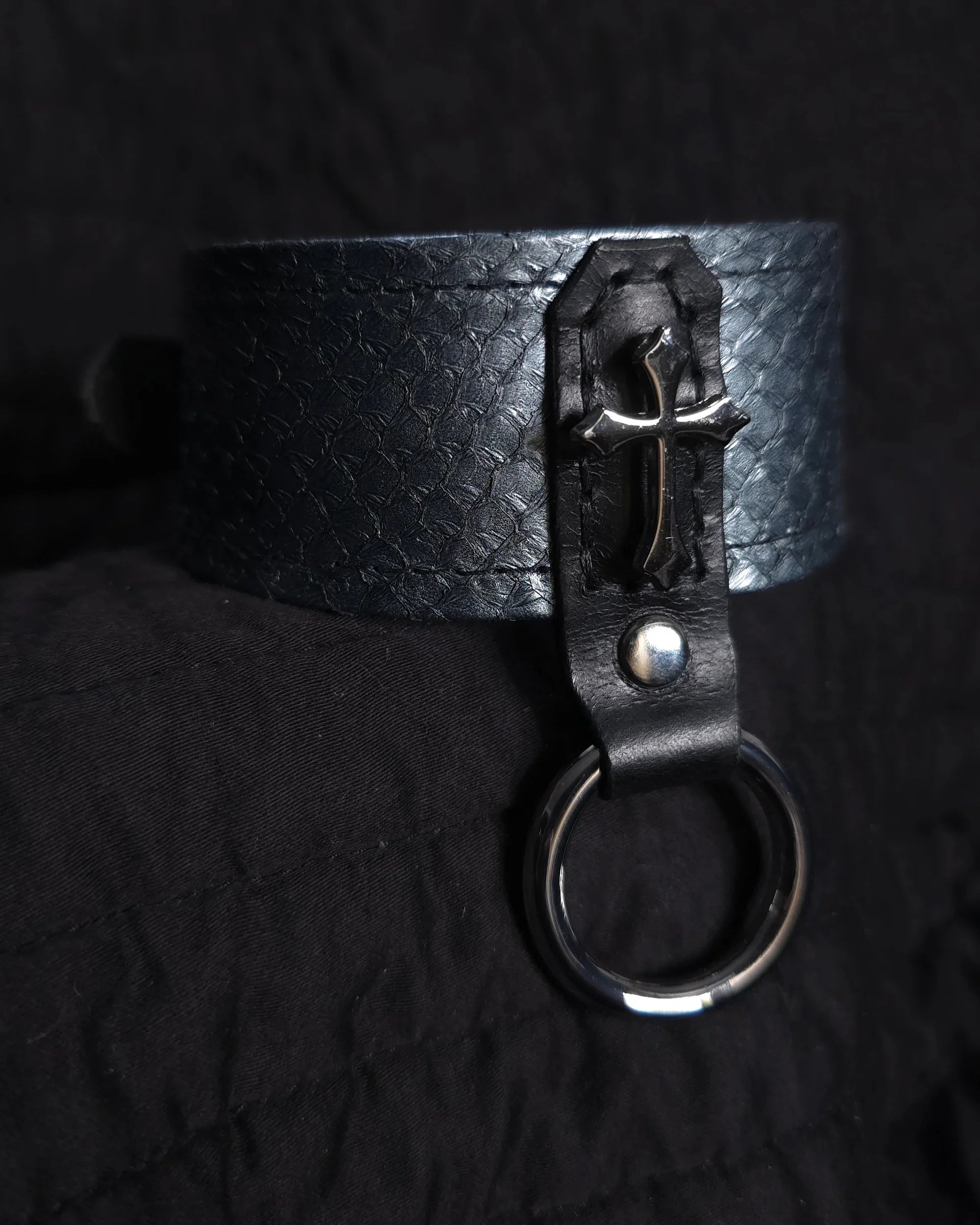 Black leather collar with a metal clasp on a dark background