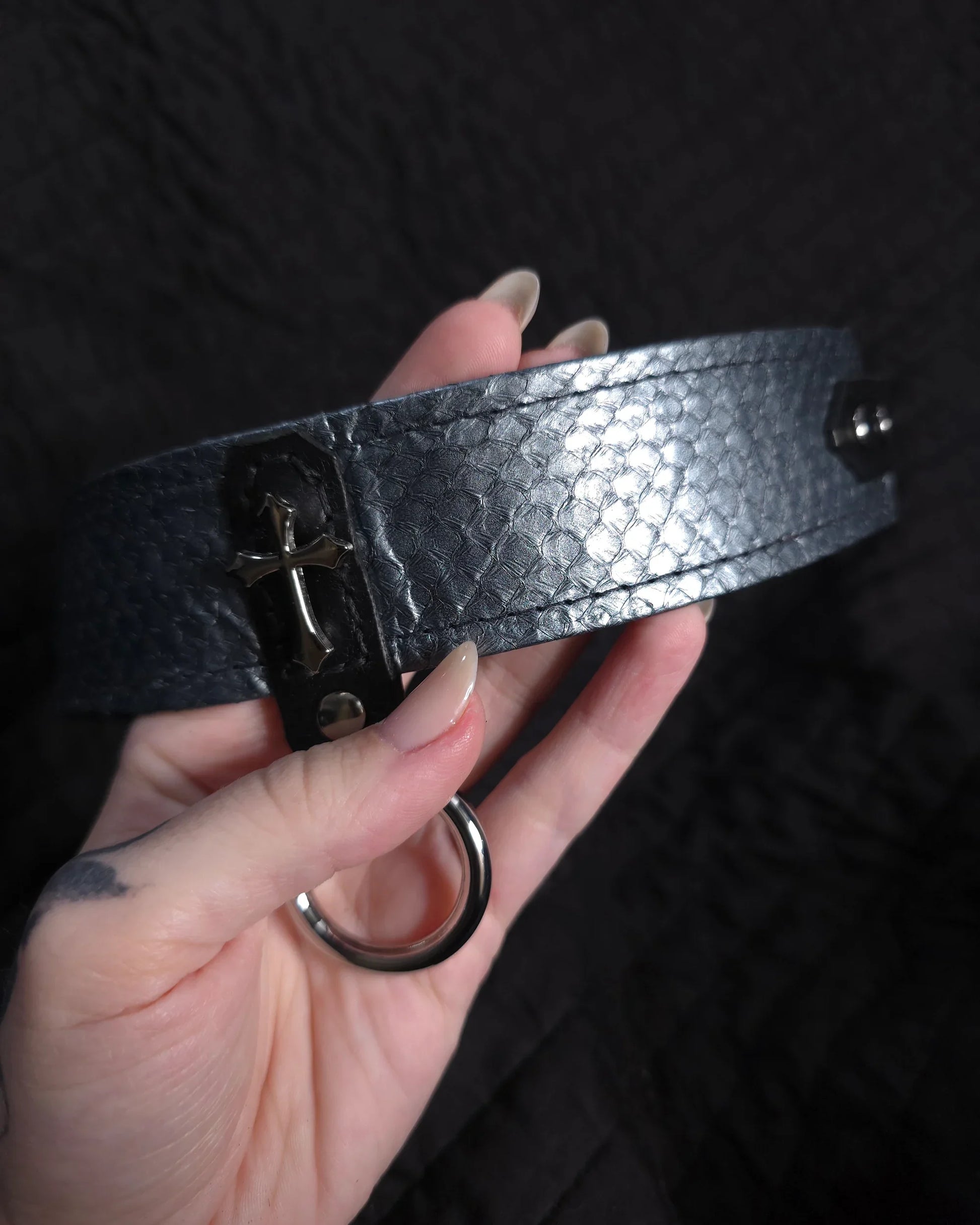 Hand holding a metallic collar with a clasp against a dark background