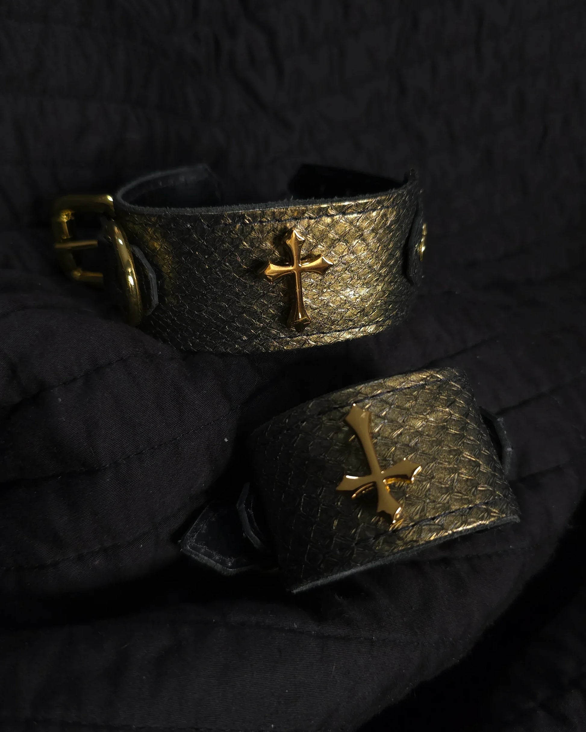 Two metallic bracelets with gold crosses on a dark textured background