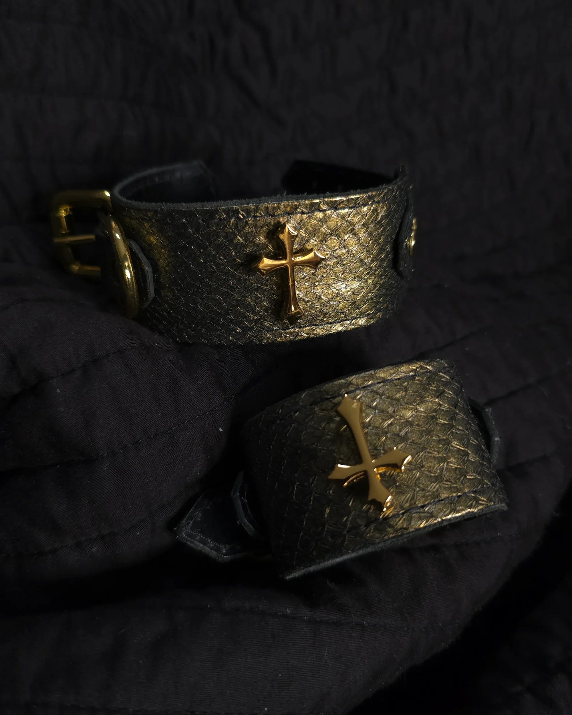 Two metallic bracelets with gold crosses on a dark textured background