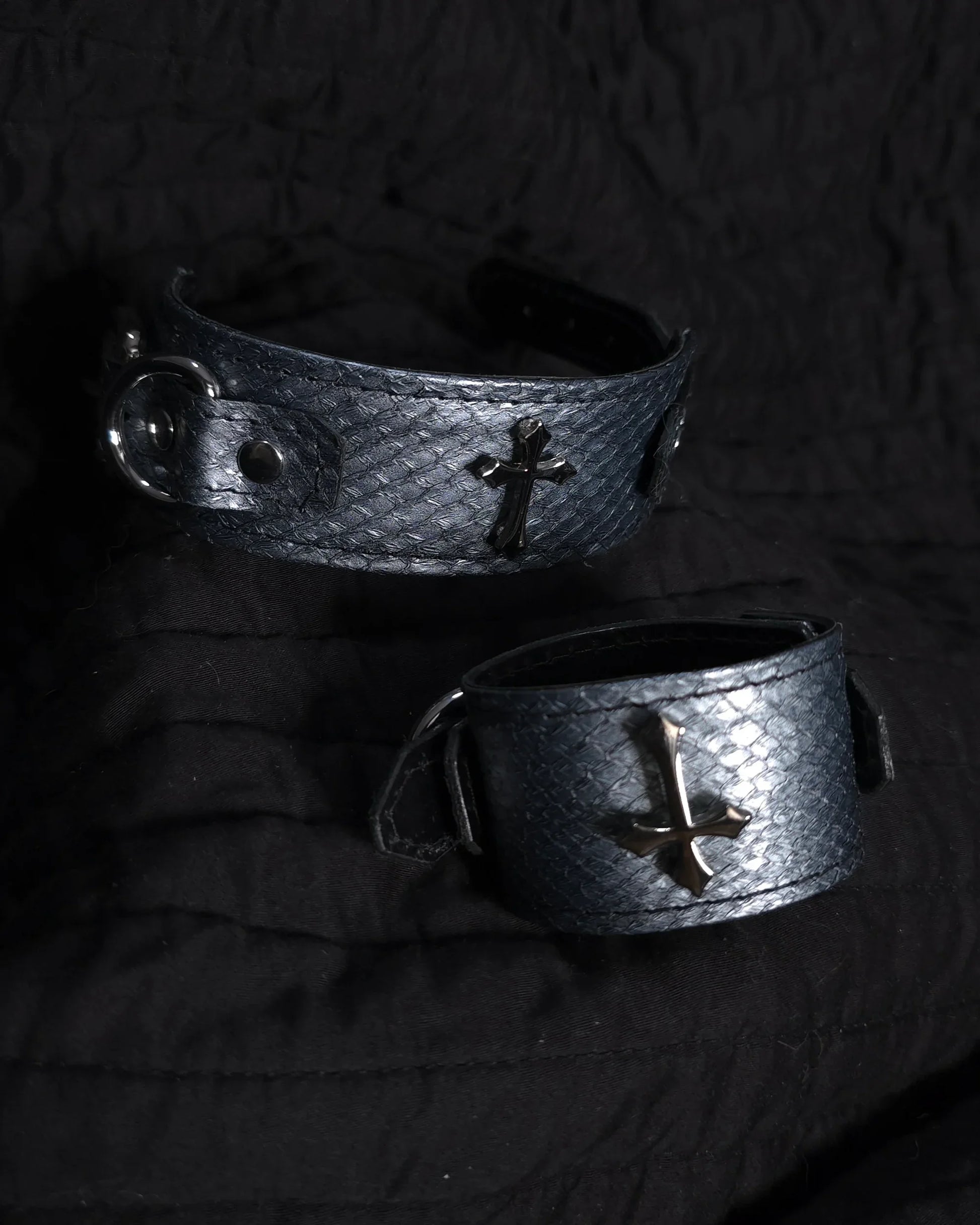 Two metallic bracelets with cross designs on a dark background
