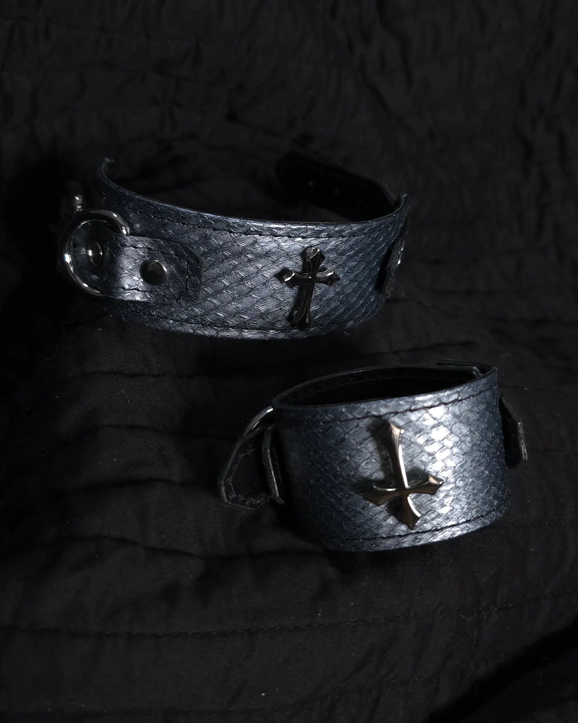 Two metallic bracelets with cross designs on a dark background