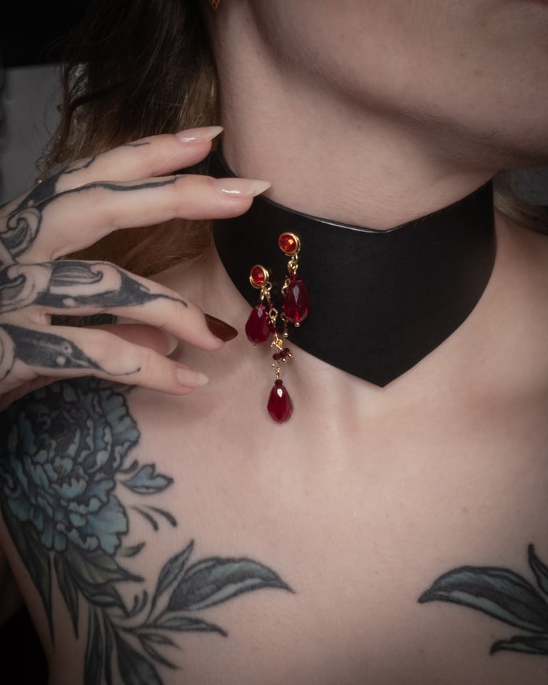 Person wearing a black choker with red teardrop-shaped beads, close-up on neck and chest.