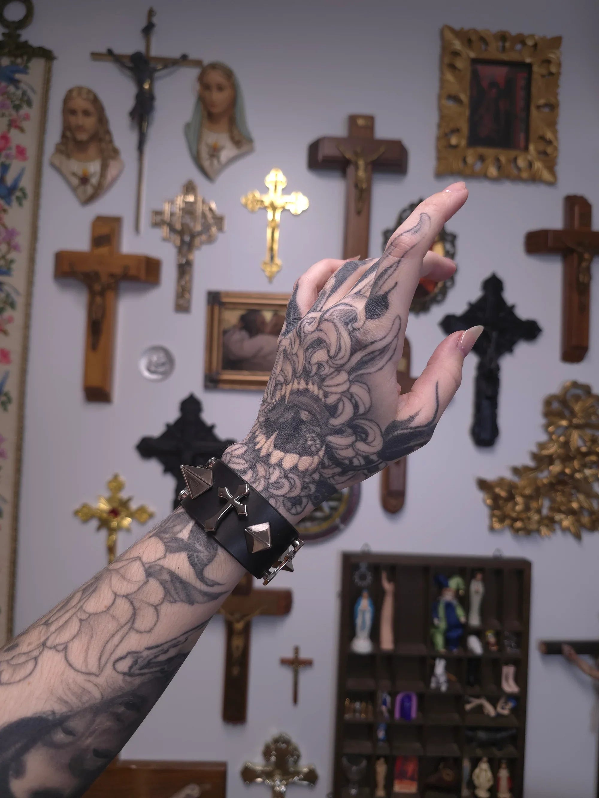 Tattooed arm with a bracelet against a wall with religious decor
