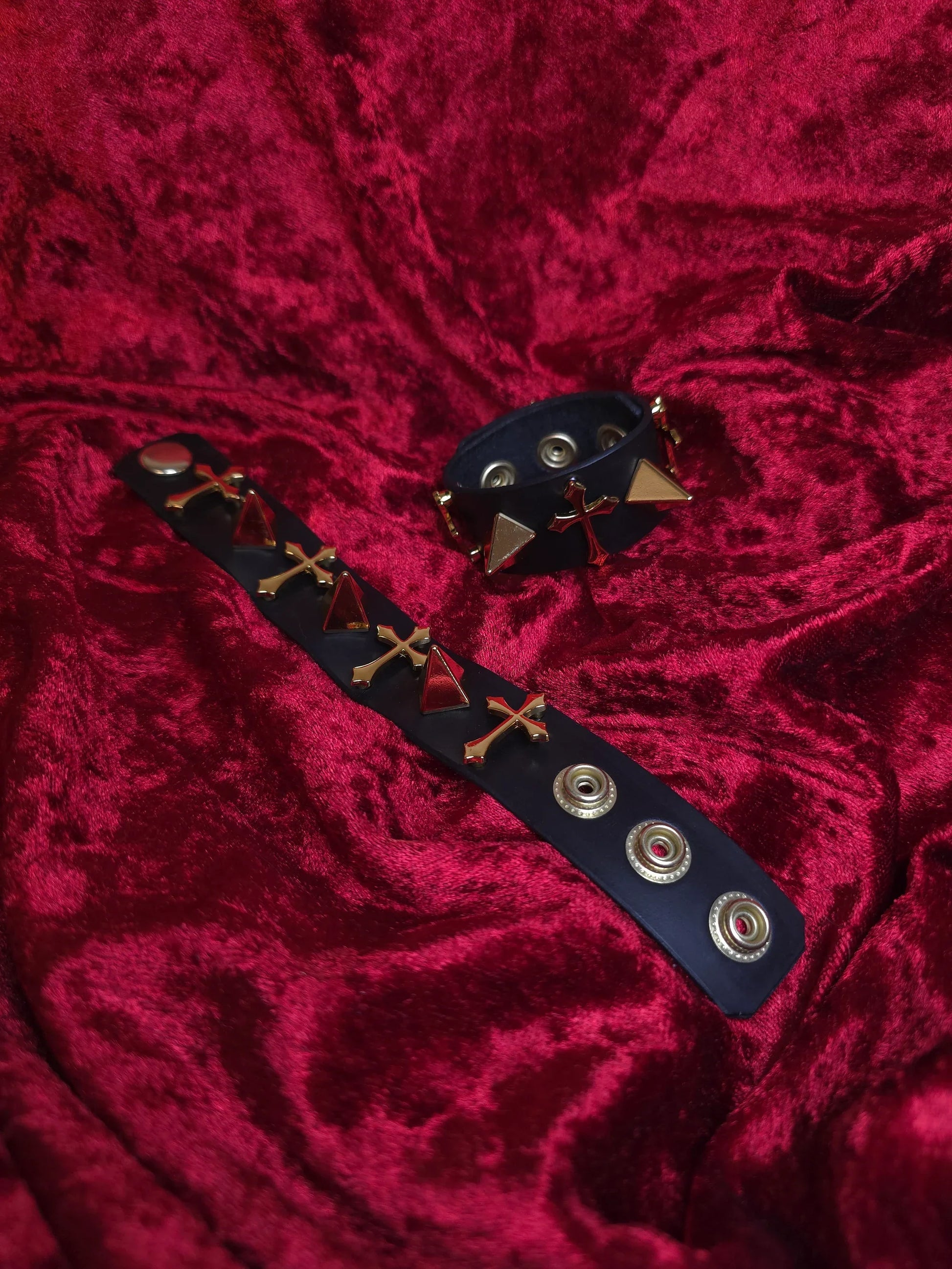 Black leather bracelet with gold accents on a red textured fabric background