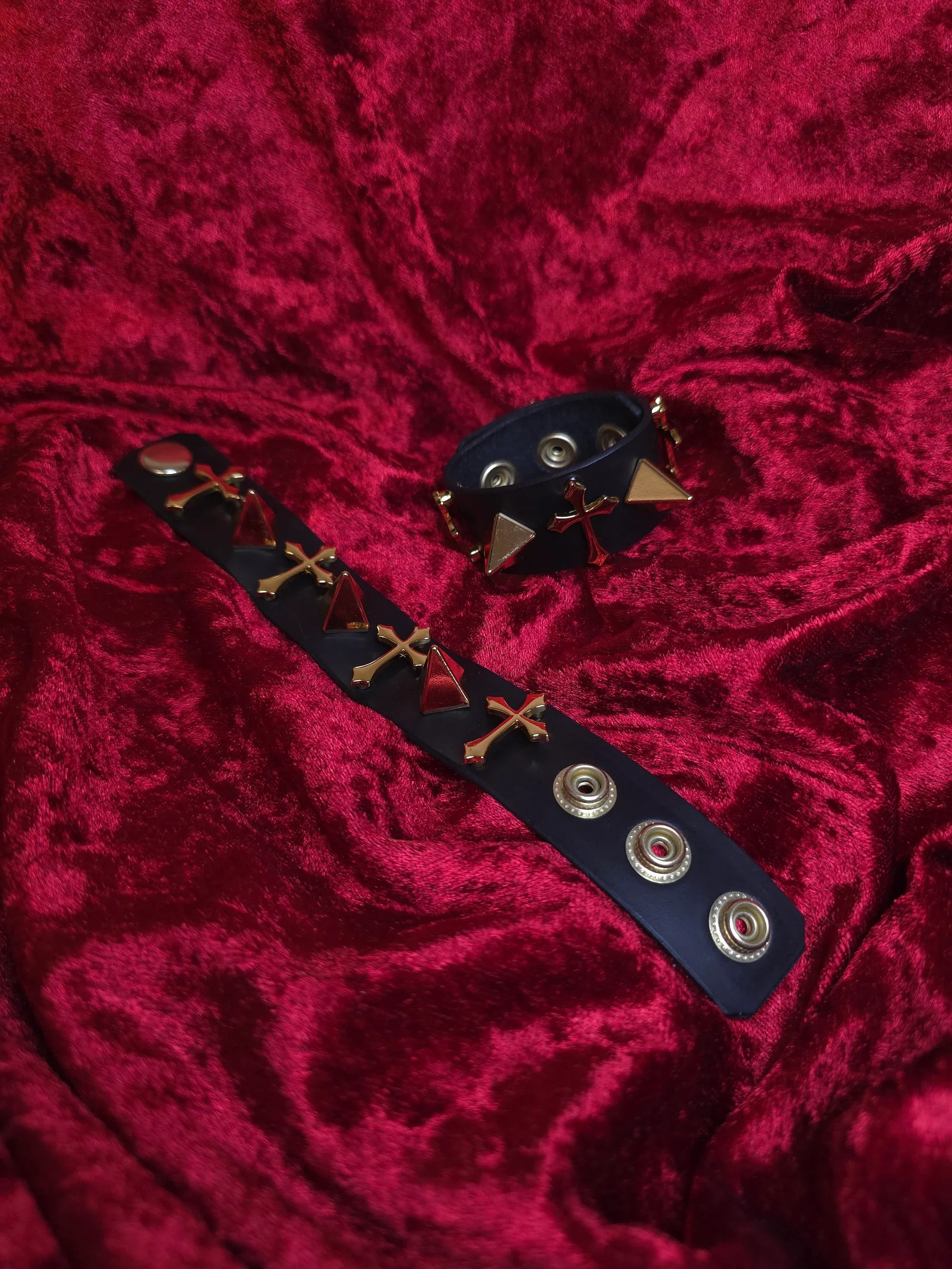 Black leather bracelet with gold accents on a red textured fabric background