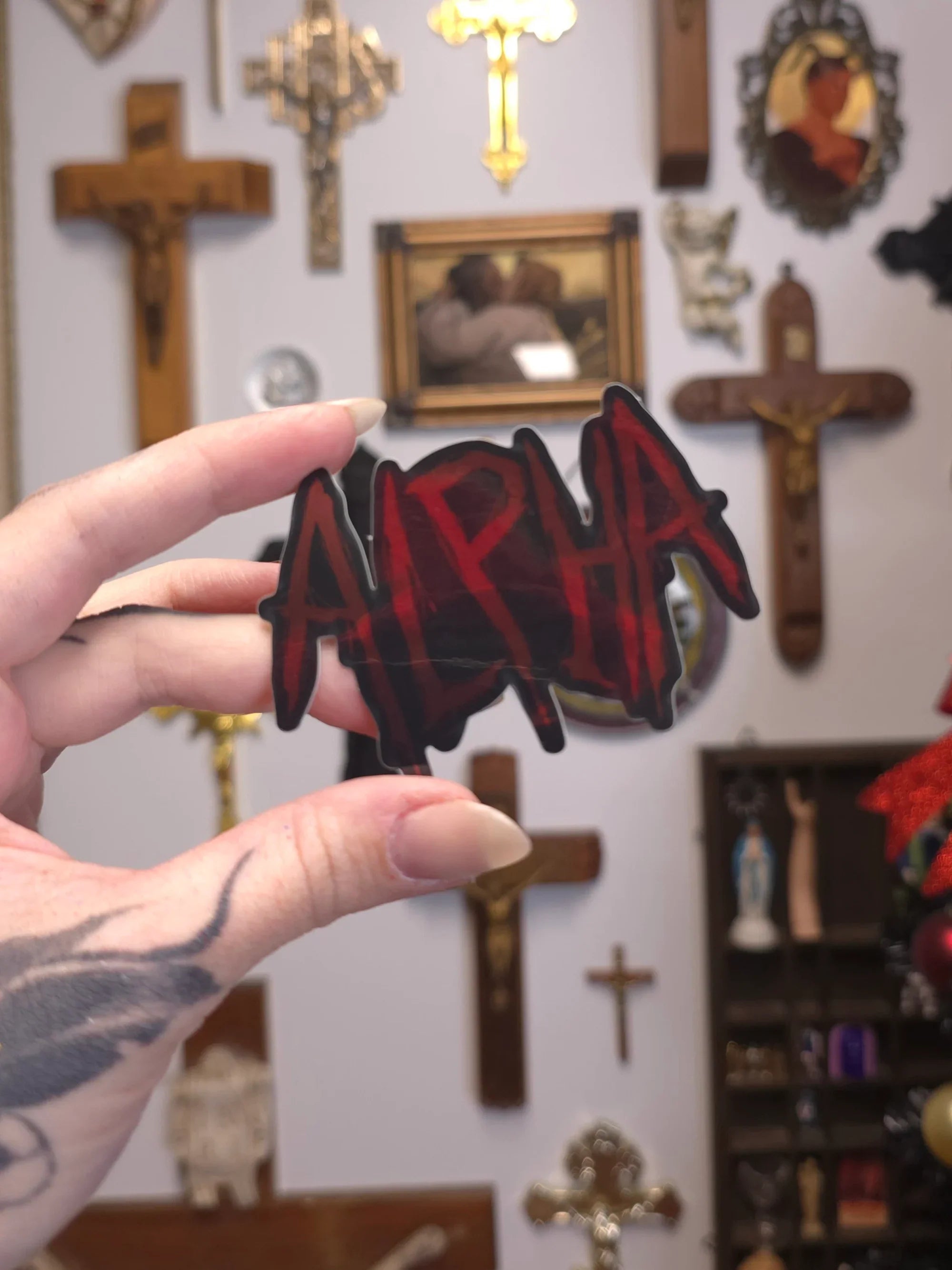 Hand holding a 'Alpha' sticker with religious decor in the background