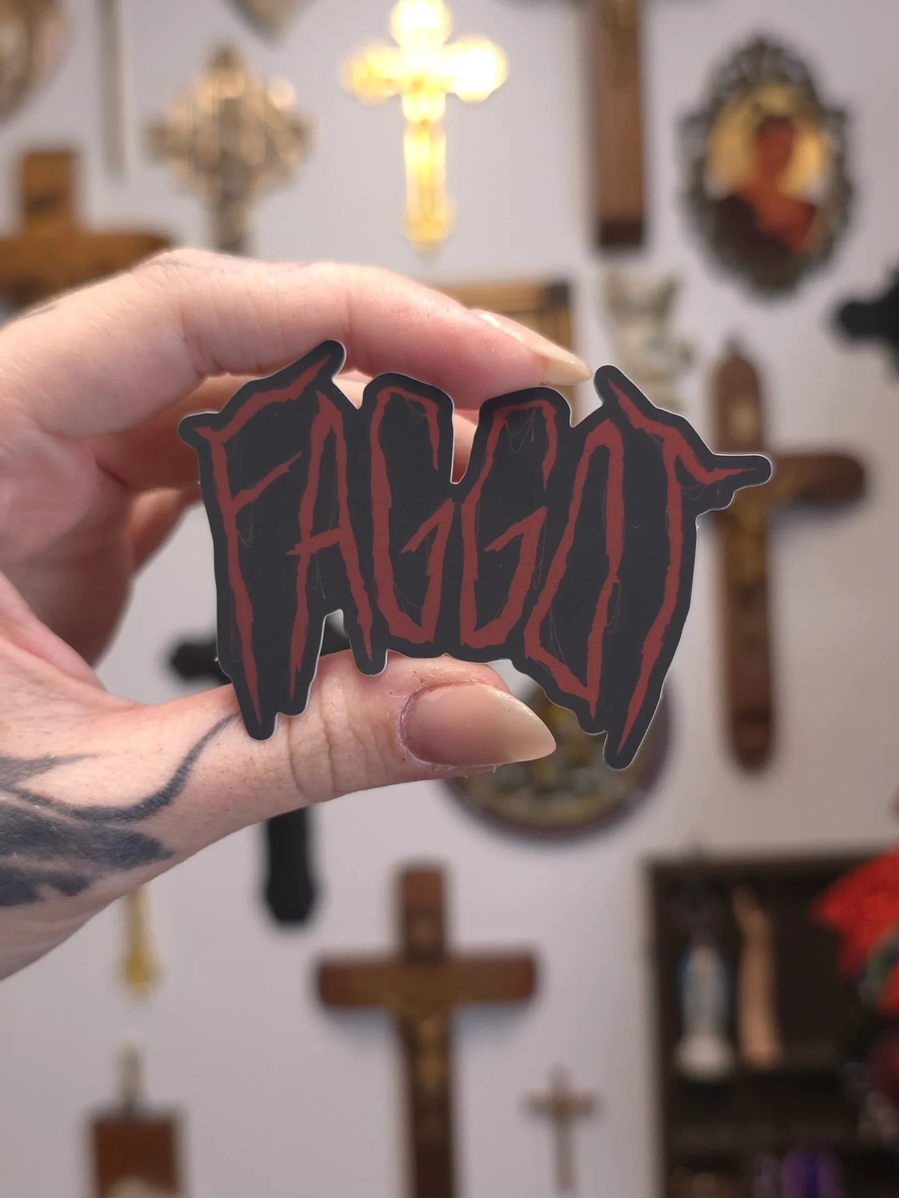 Hand holding a 'FAGGOT' sticker on blurry background