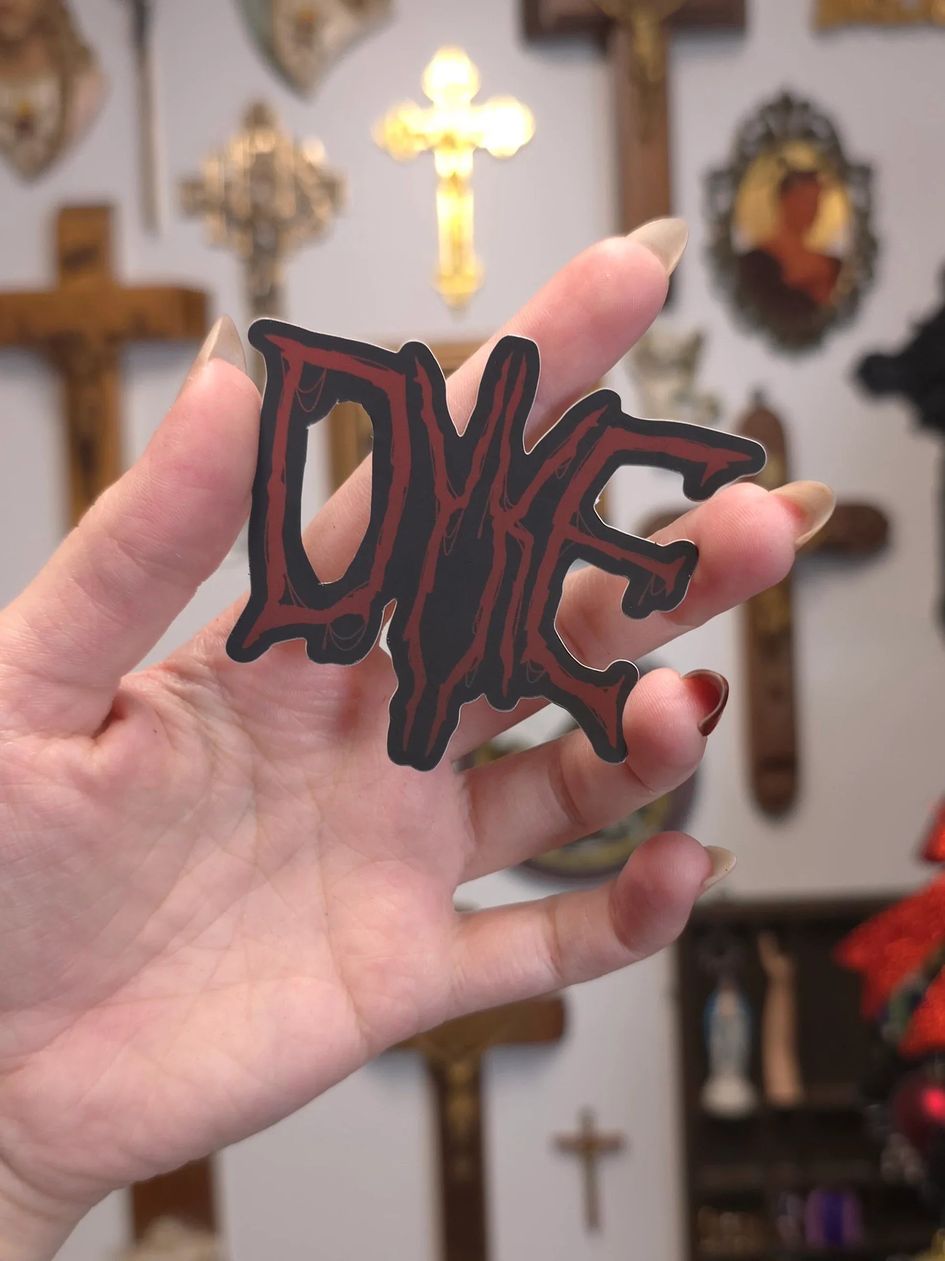 Hand holding a 'DYKE' sticker on a blurry background