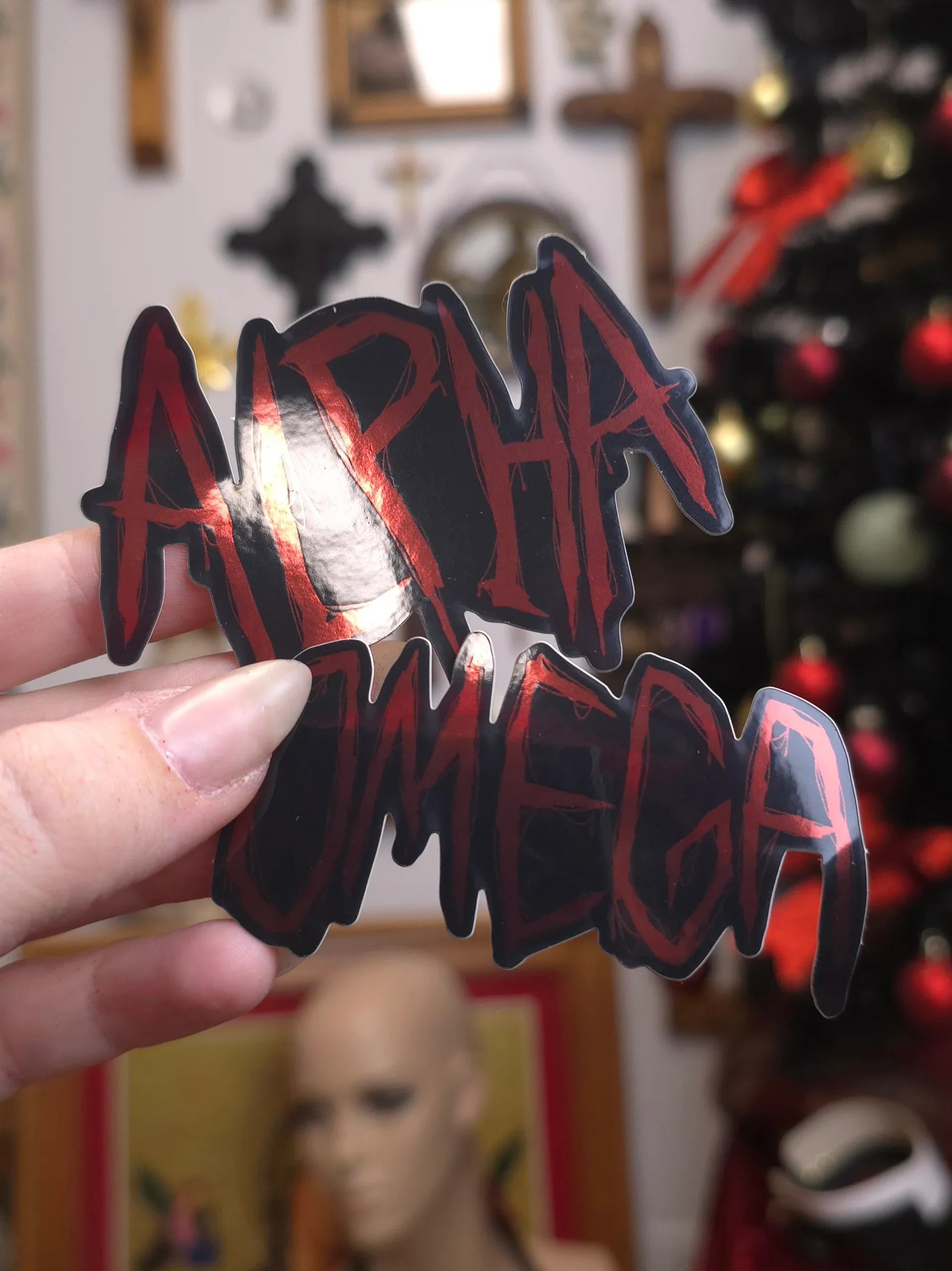 Hand holding a 'Alpha Omega' sticker with a blurred background