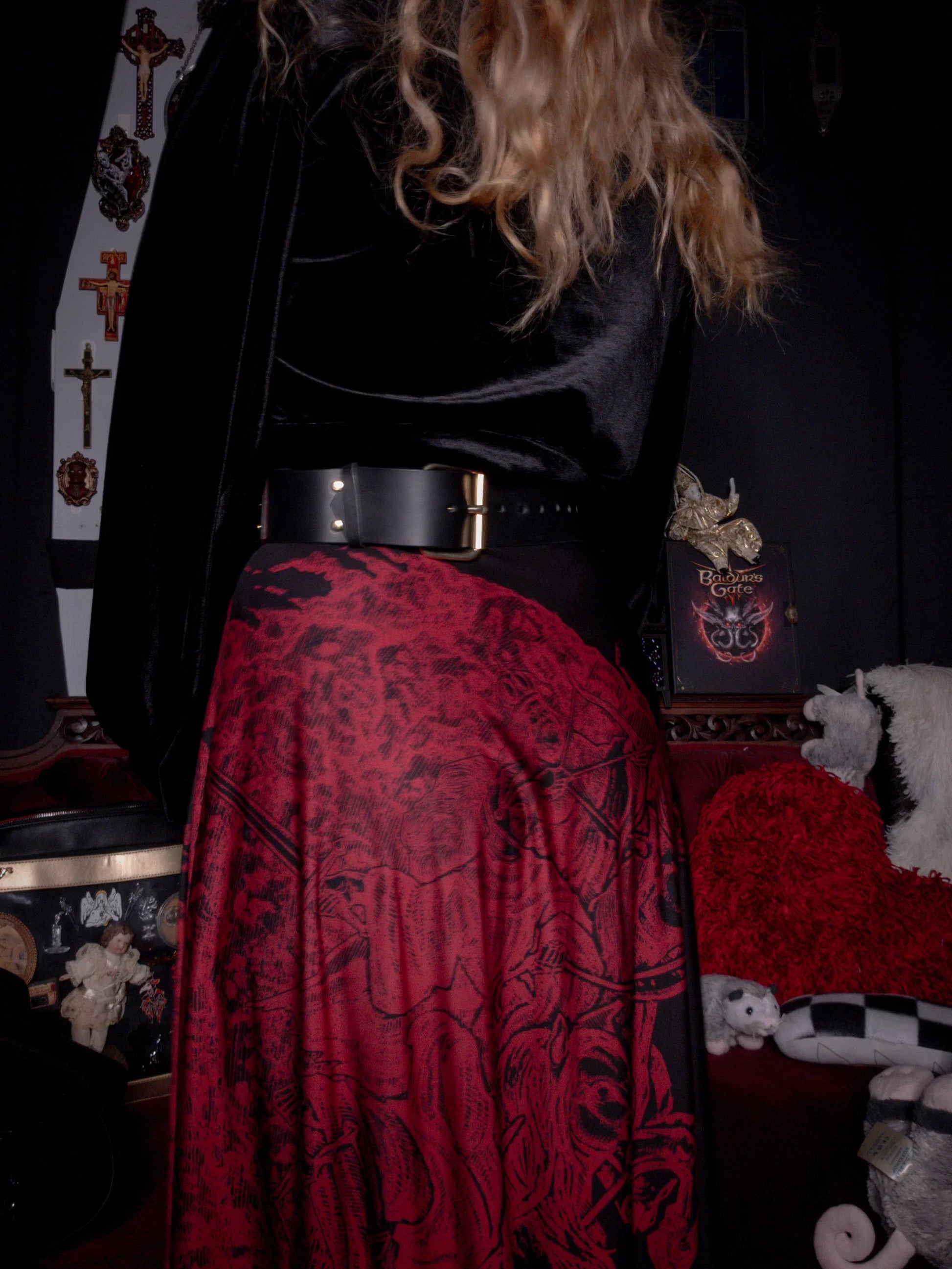 Person wearing a black top and red patterned skirt in a dark room with decorative items.