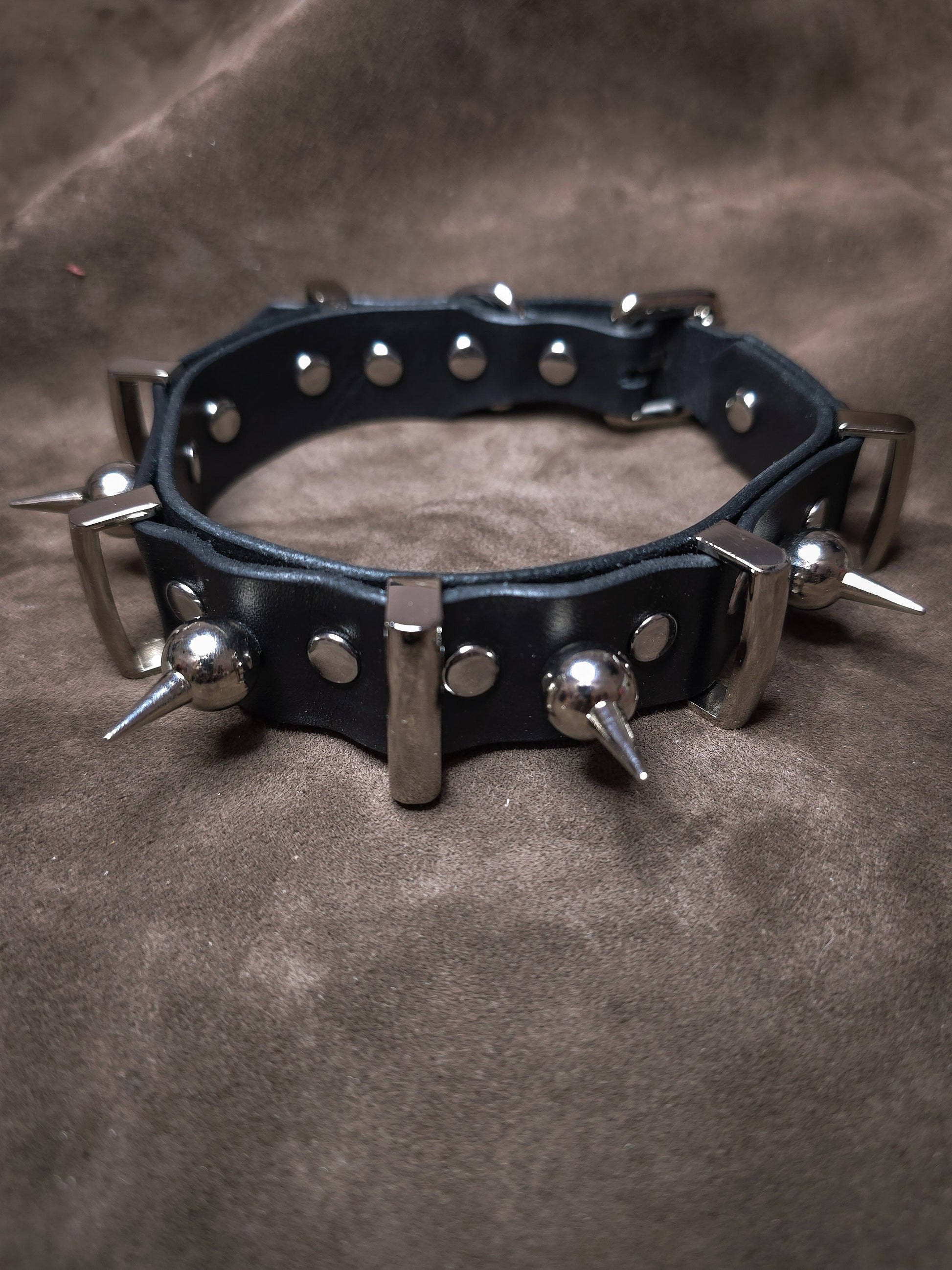 Black leather collar with metal spikes on a brown background