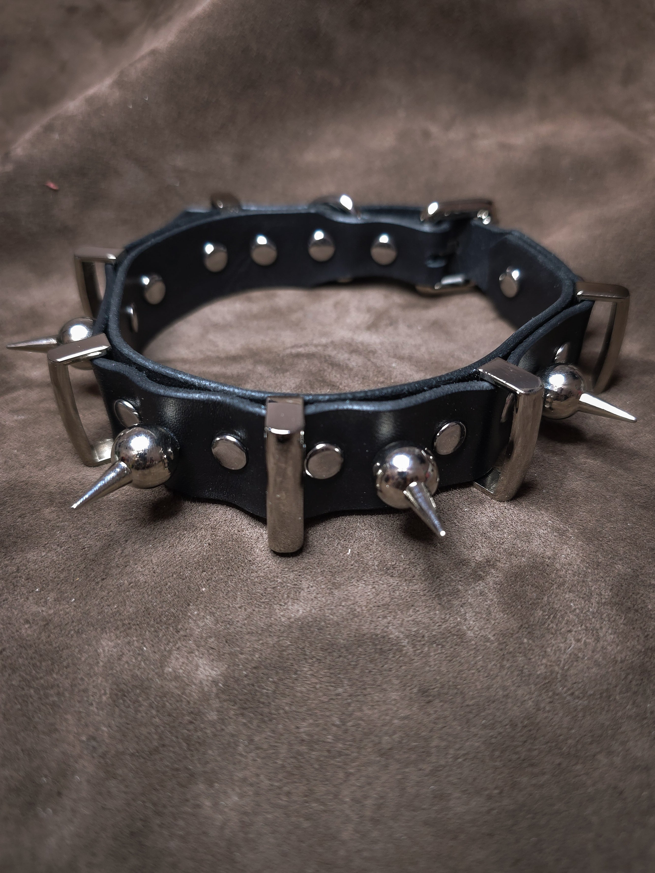Black leather collar with metal spikes on a brown background