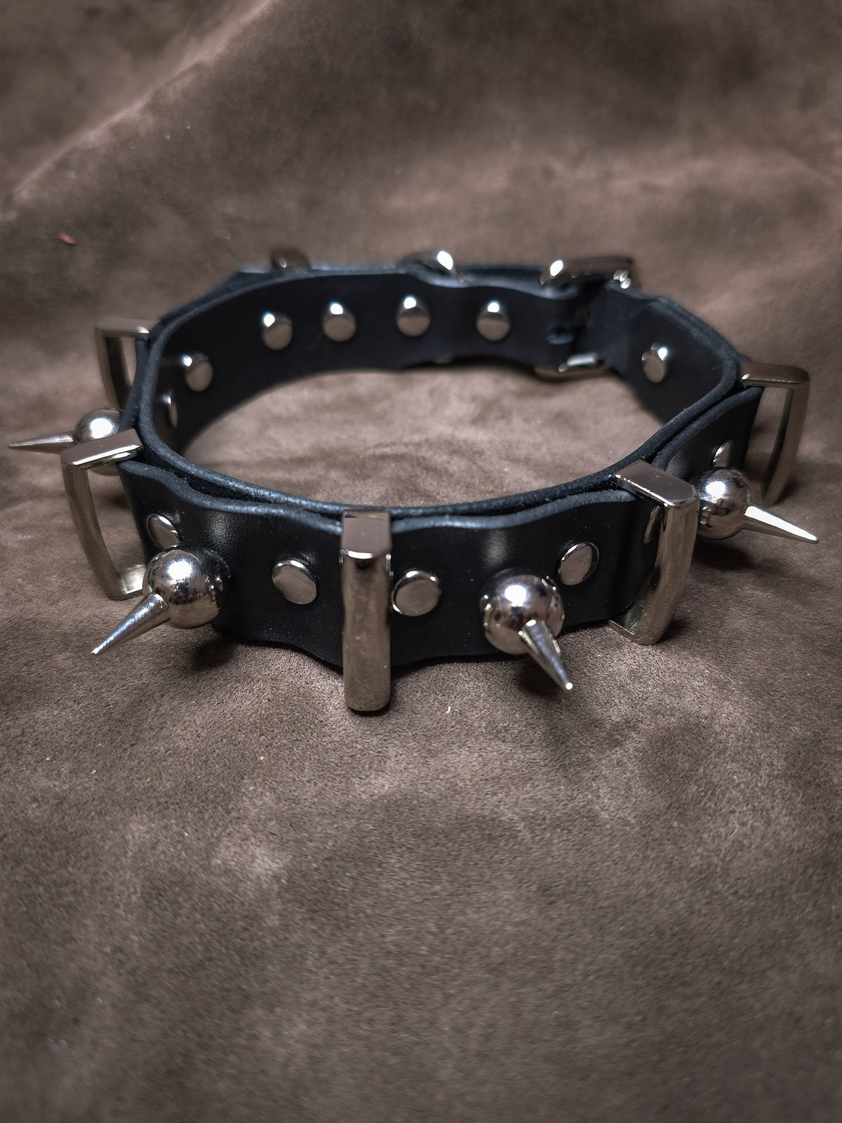 Black leather collar with metal spikes on a brown background