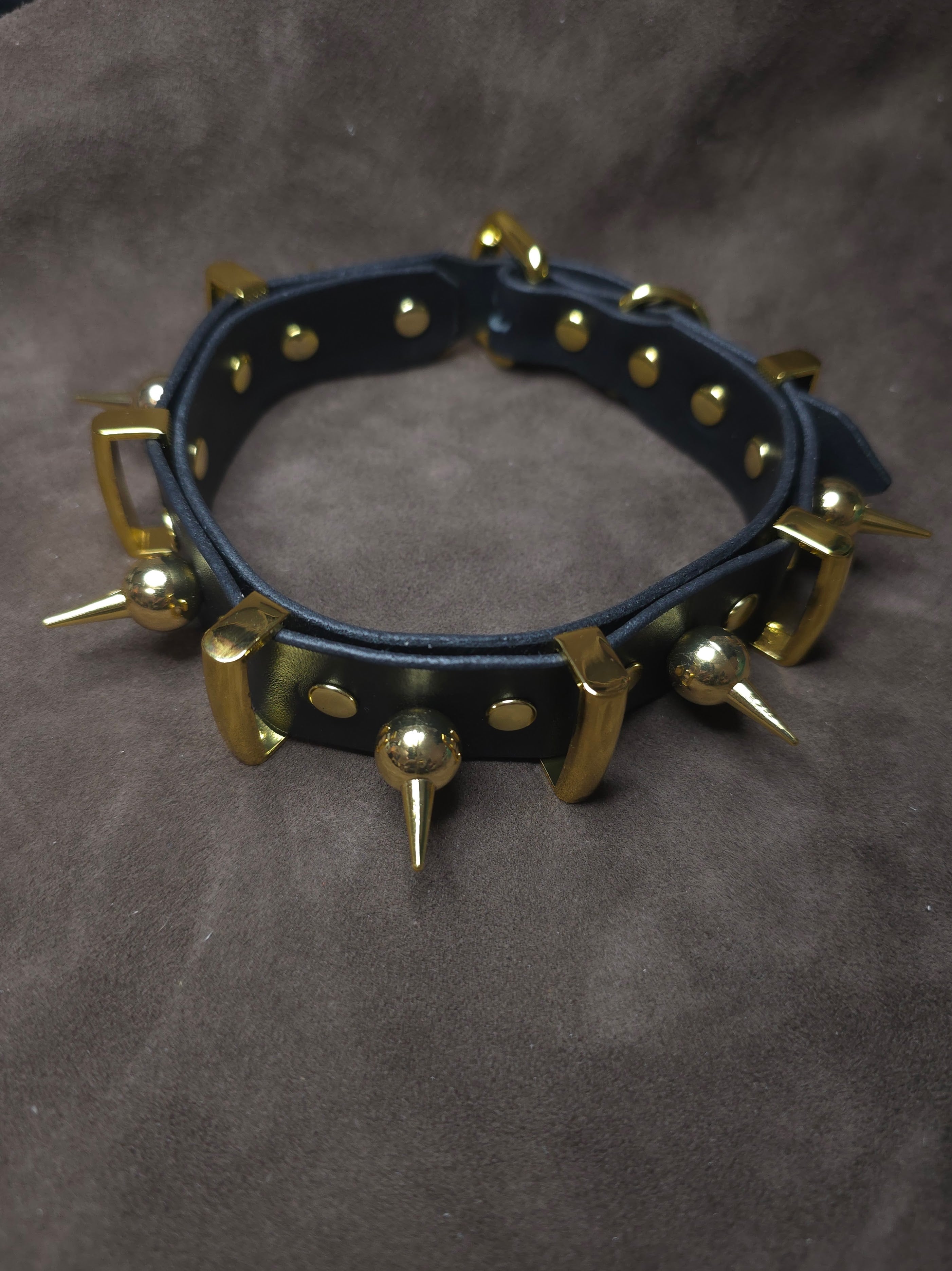 Black leather collar with gold spikes on a gray background