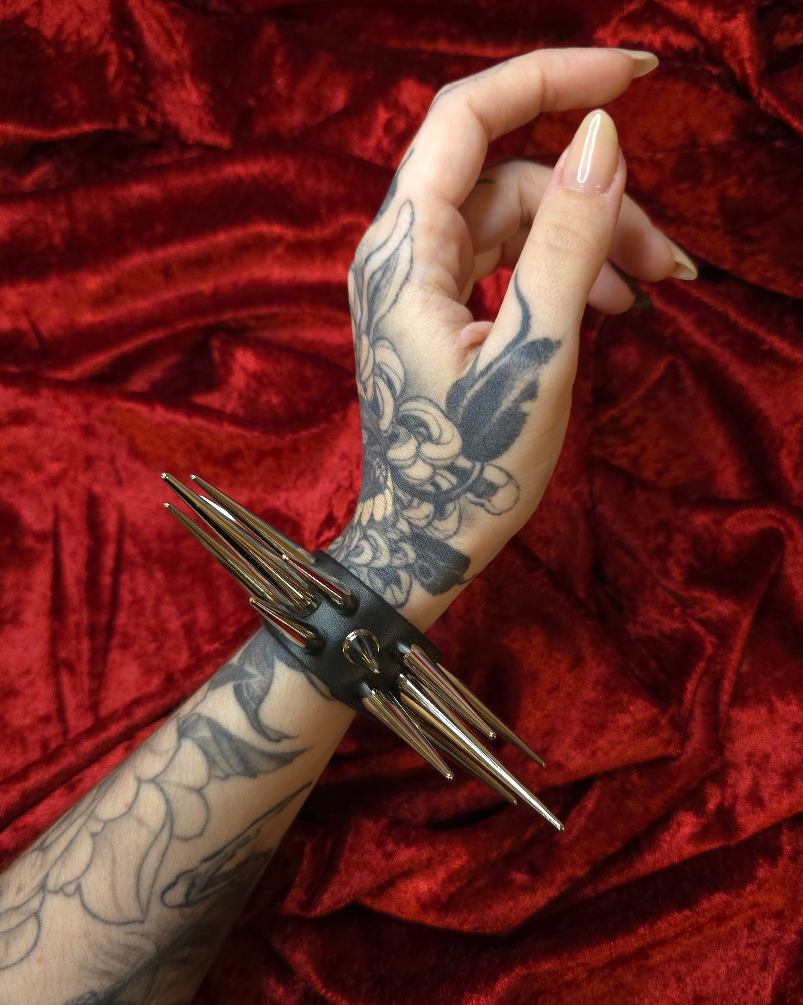 Hand with tattoos wearing spiked cuff against a red velvet background