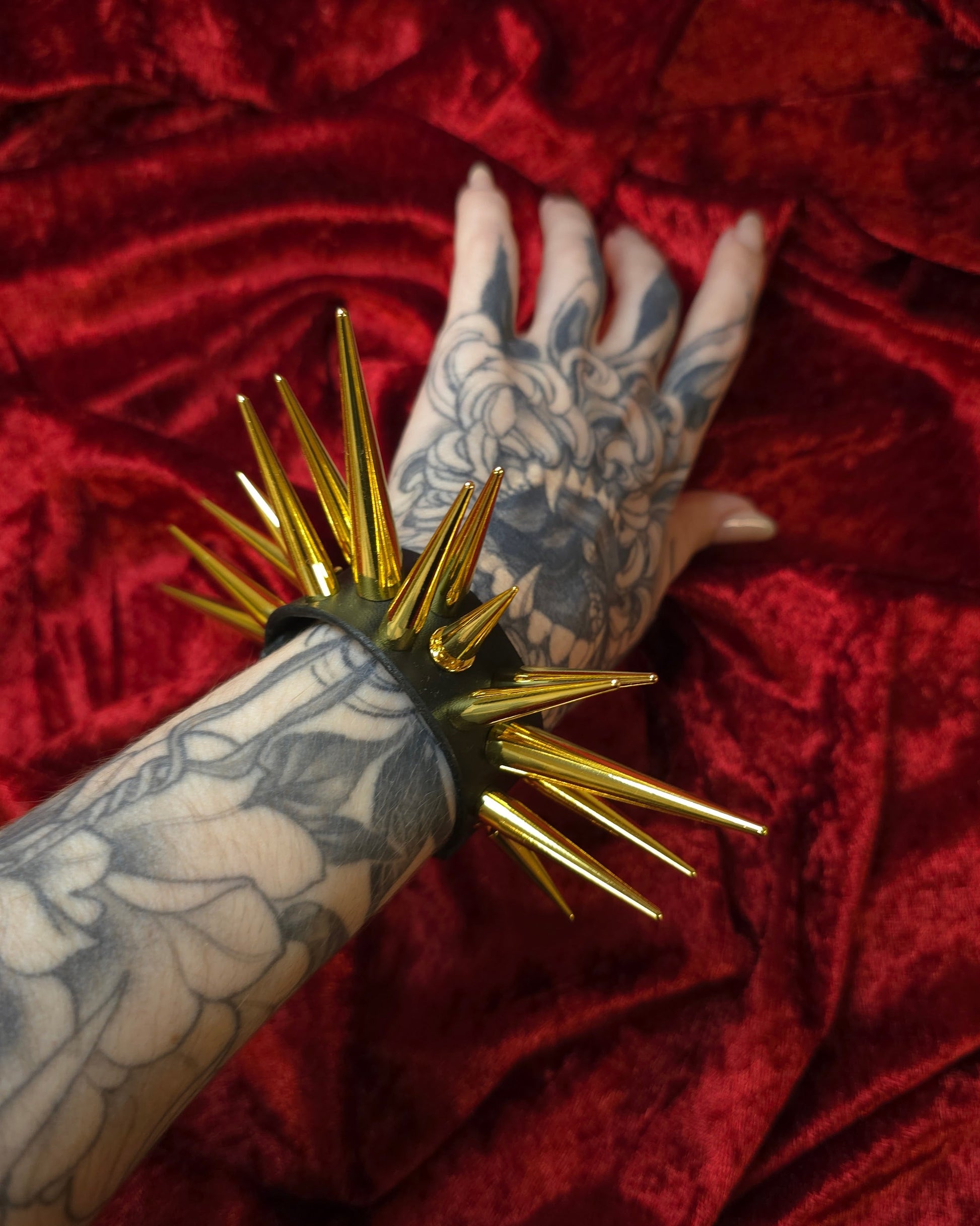 Hand with tattoos holding a gold spiked cuff against a red velvet background