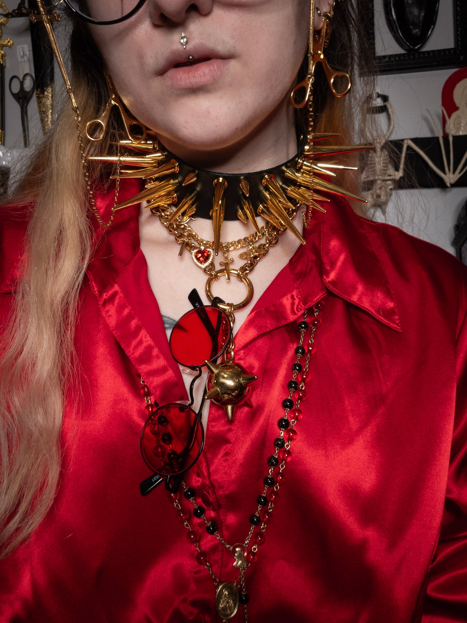 Person wearing a red satin shirt and elaborate gold jewelry with a blurred background