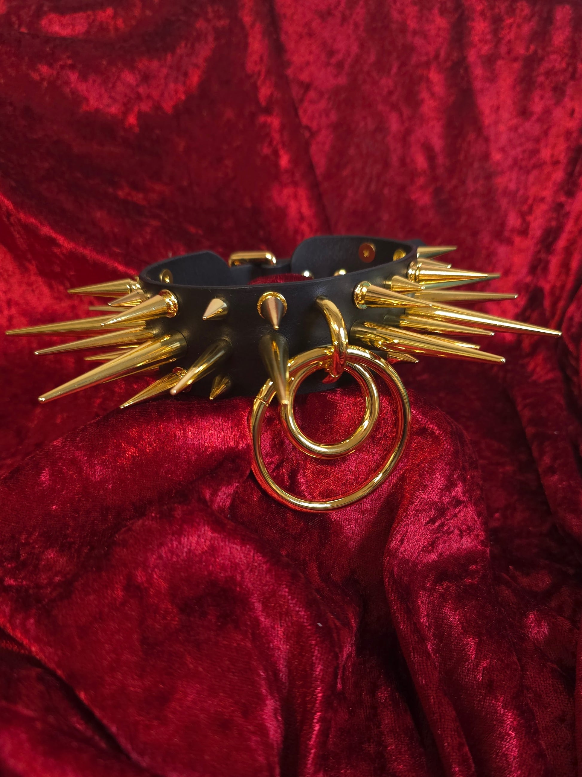 Black leather collar with gold spikes on a red velvet background