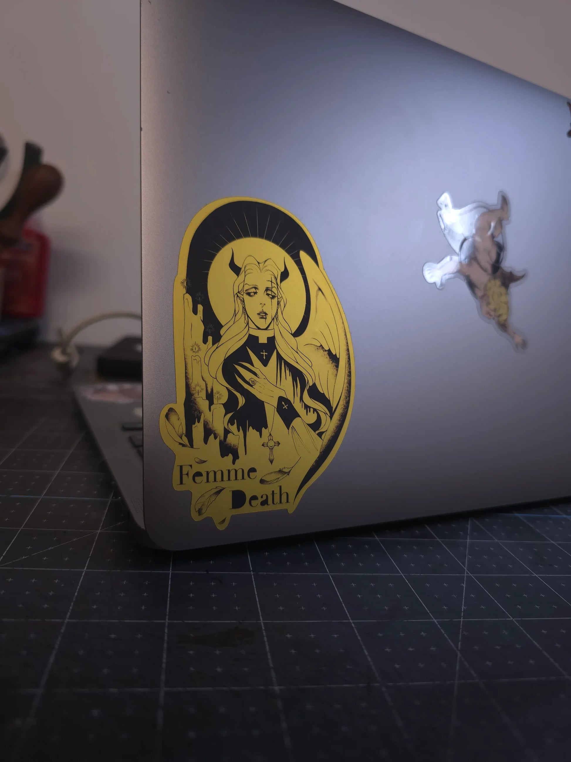 Laptop with a 'Femme Death' sticker on a dark surface