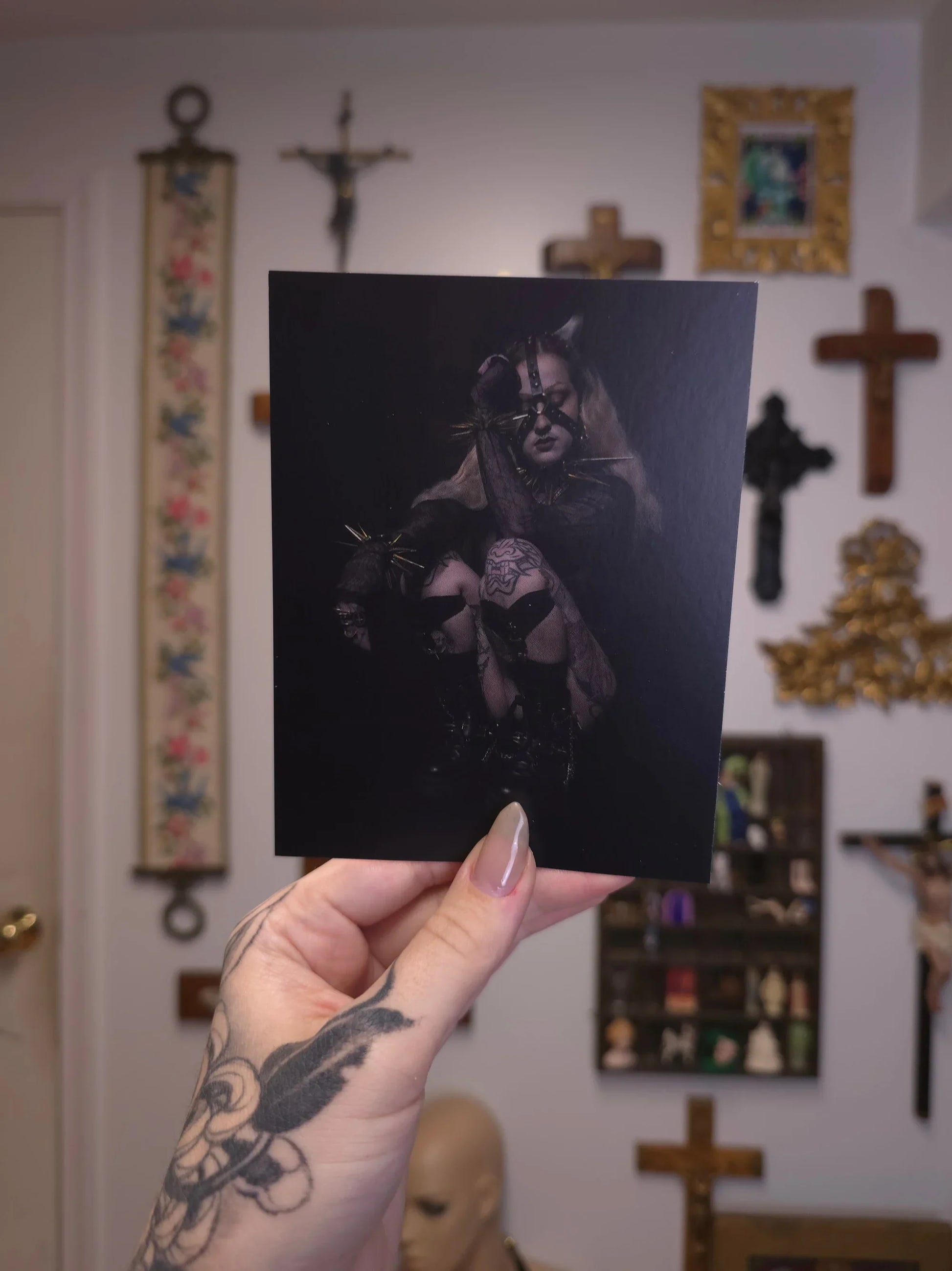 hand holding postcard with dark portrait print, against a wall with gothic decor
