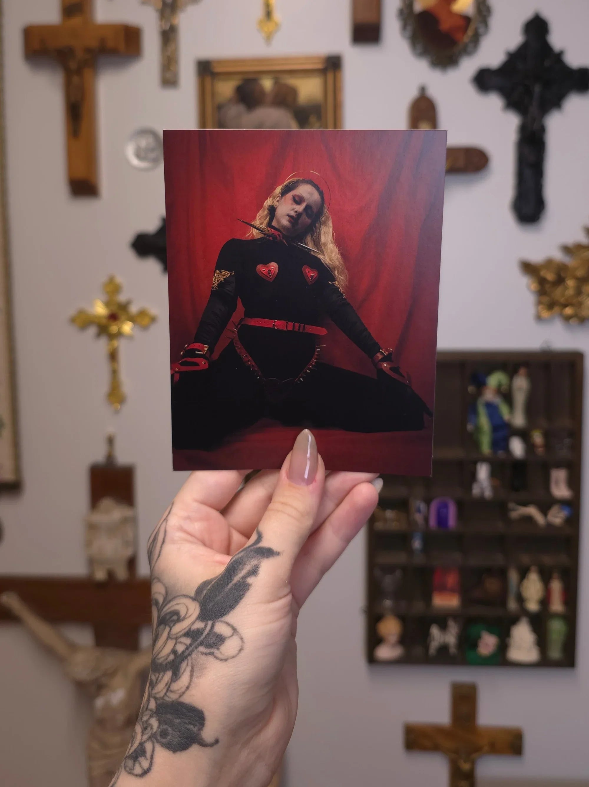 Hand holding a card with a person in a black outfit against a red curtain, against a wall with gothic decor