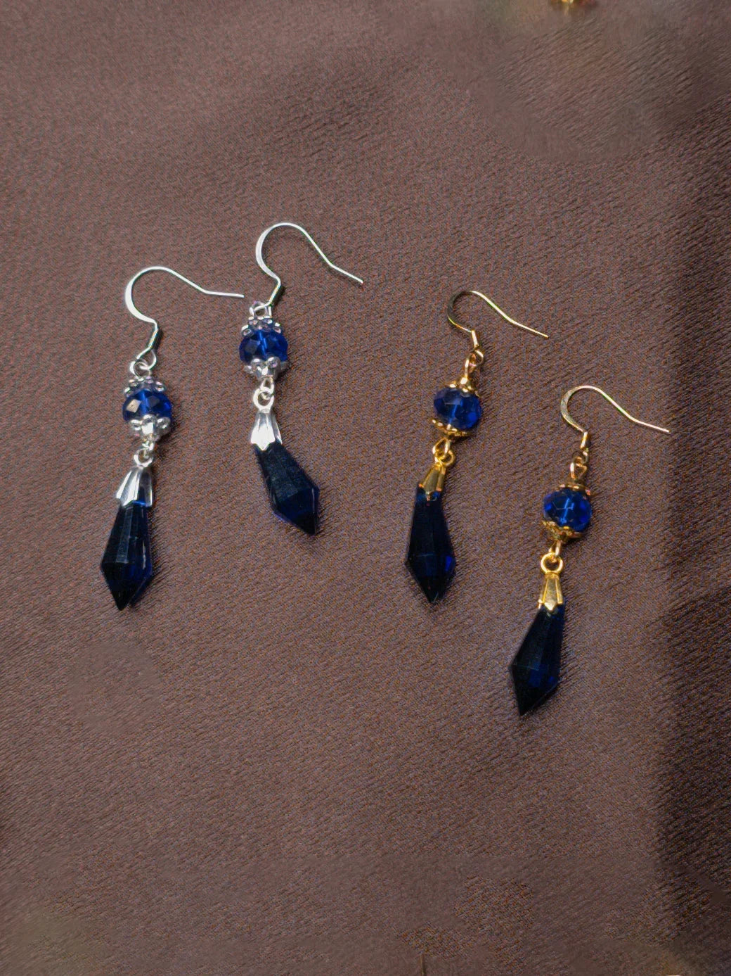 Two pairs of blue drop earrings on a brown surface
