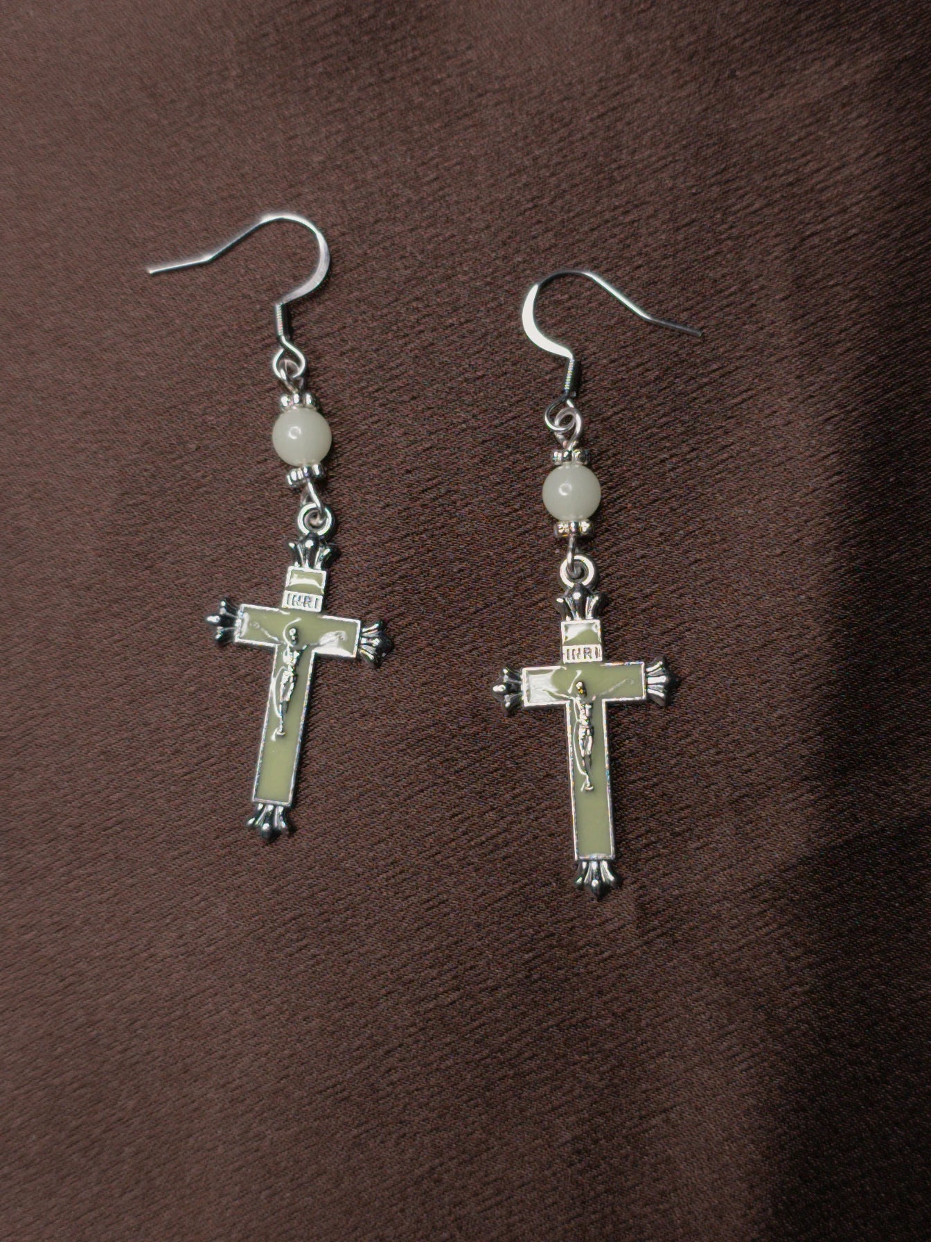 Pair of light green crucifix earrings on brown background