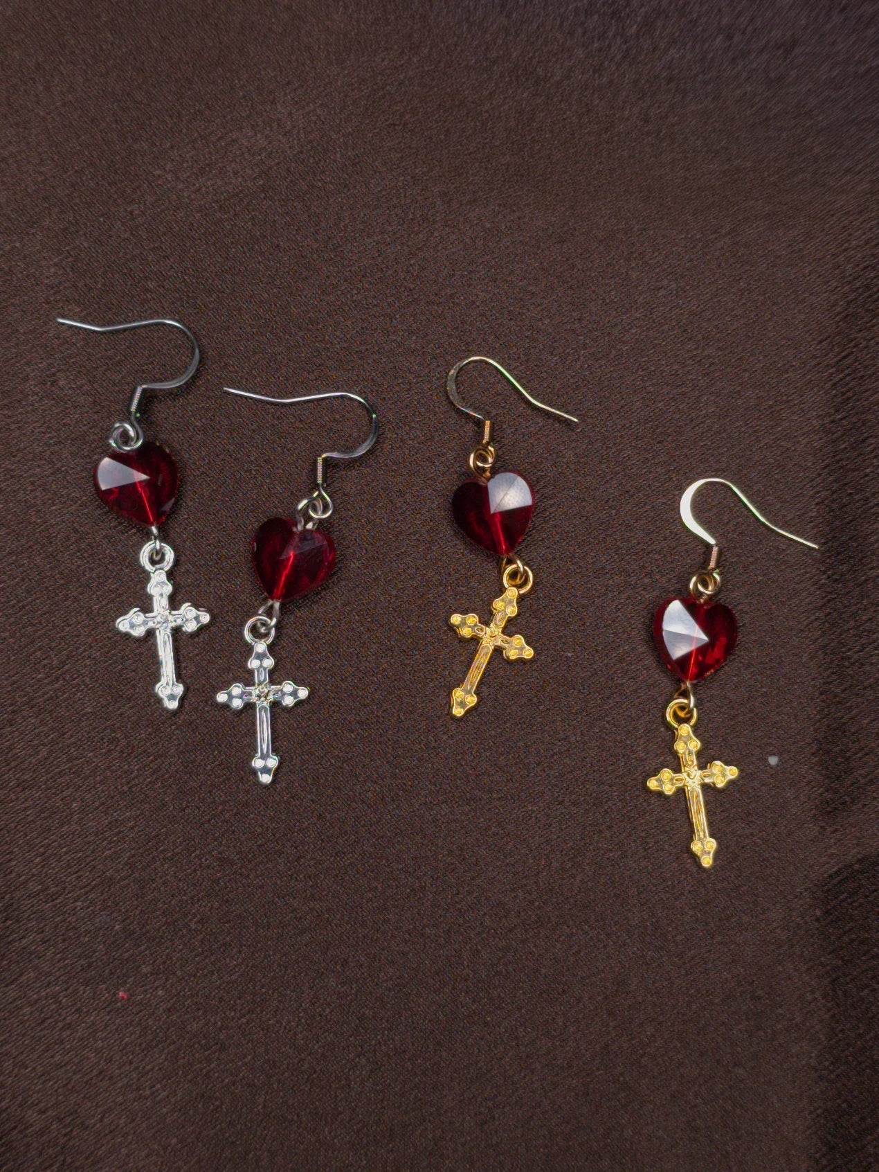 Two pairs of earrings with crosses and heart shaped beads on a brown background