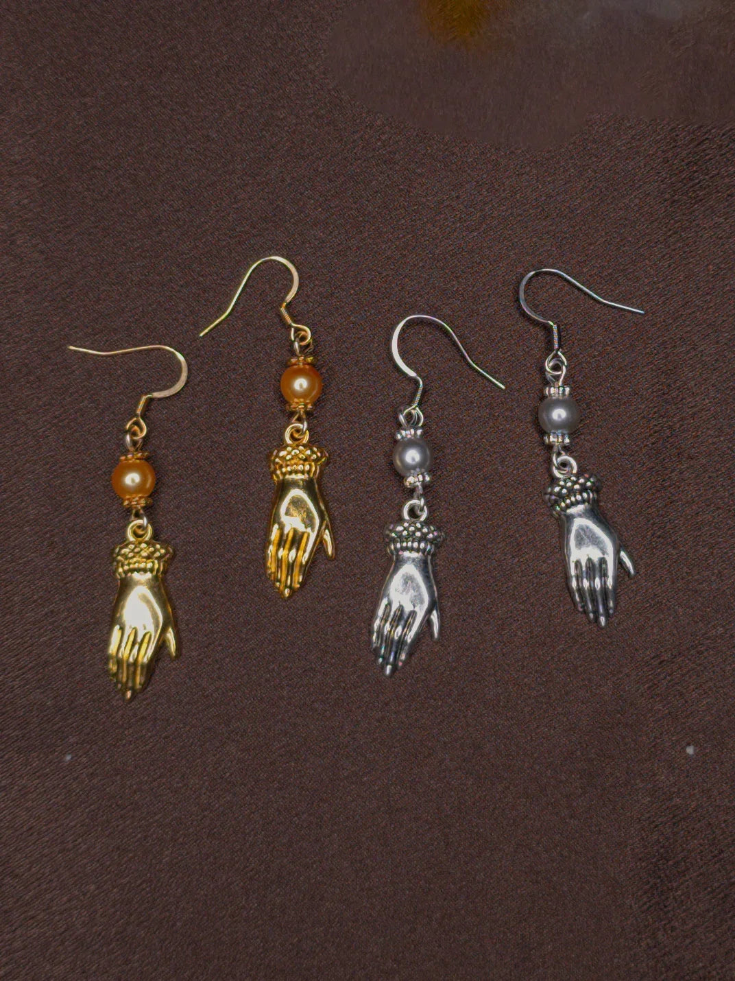 Two pairs of hand-shaped earrings on a brown background