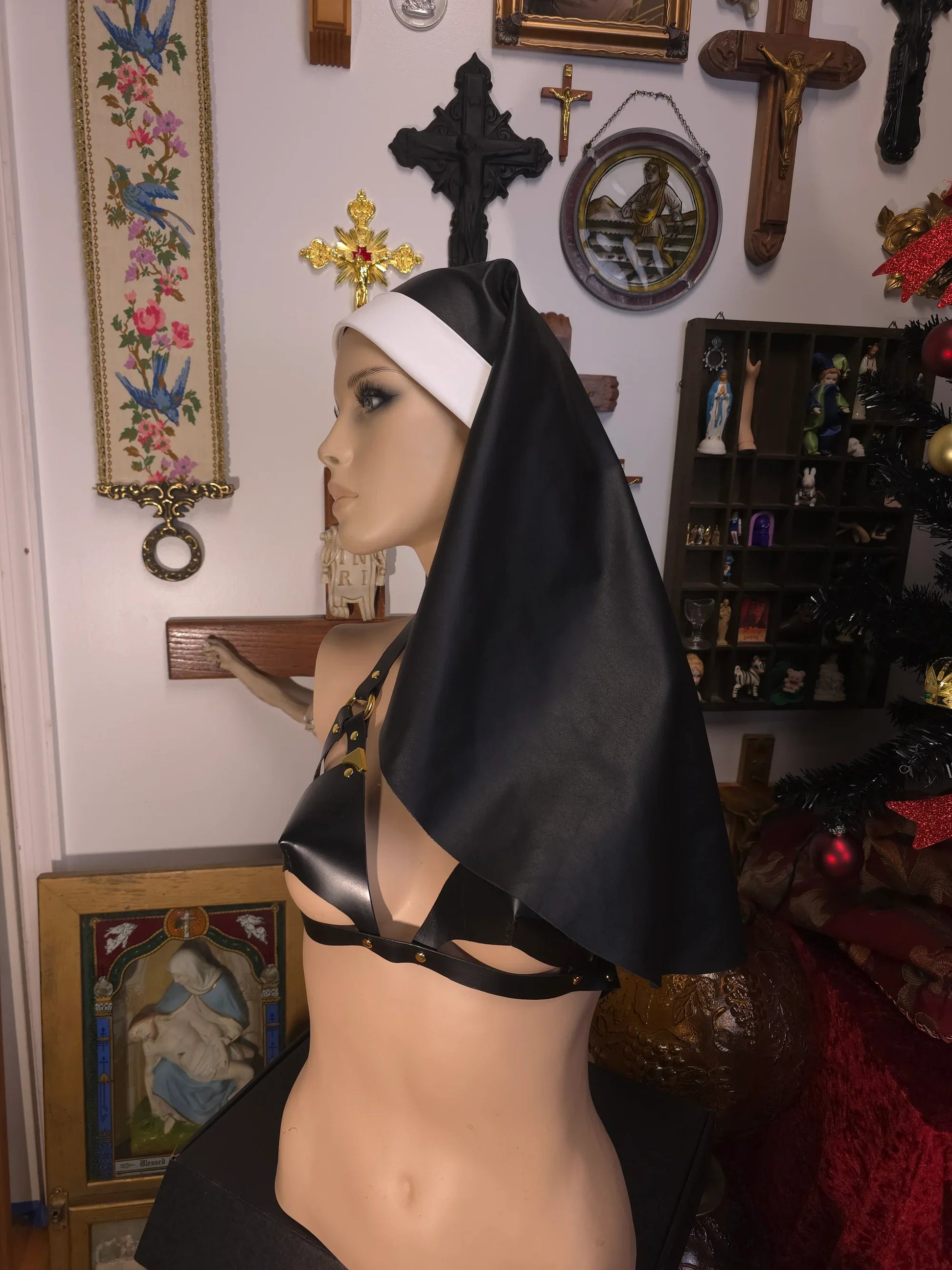 Mannequin wearing a black nun veil and bra in a room with religious decor.