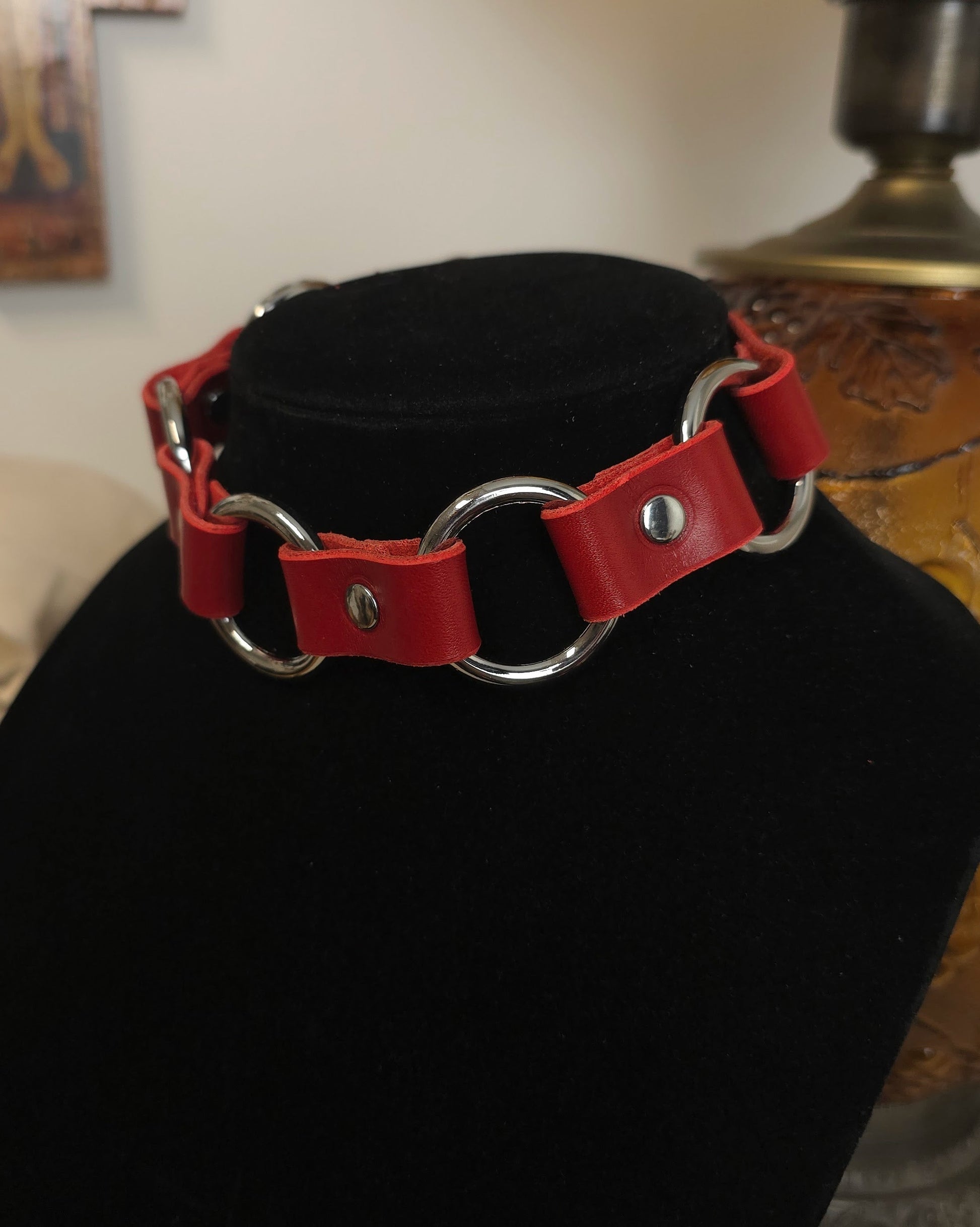 Red leather collar with silver hardware on a black stand.