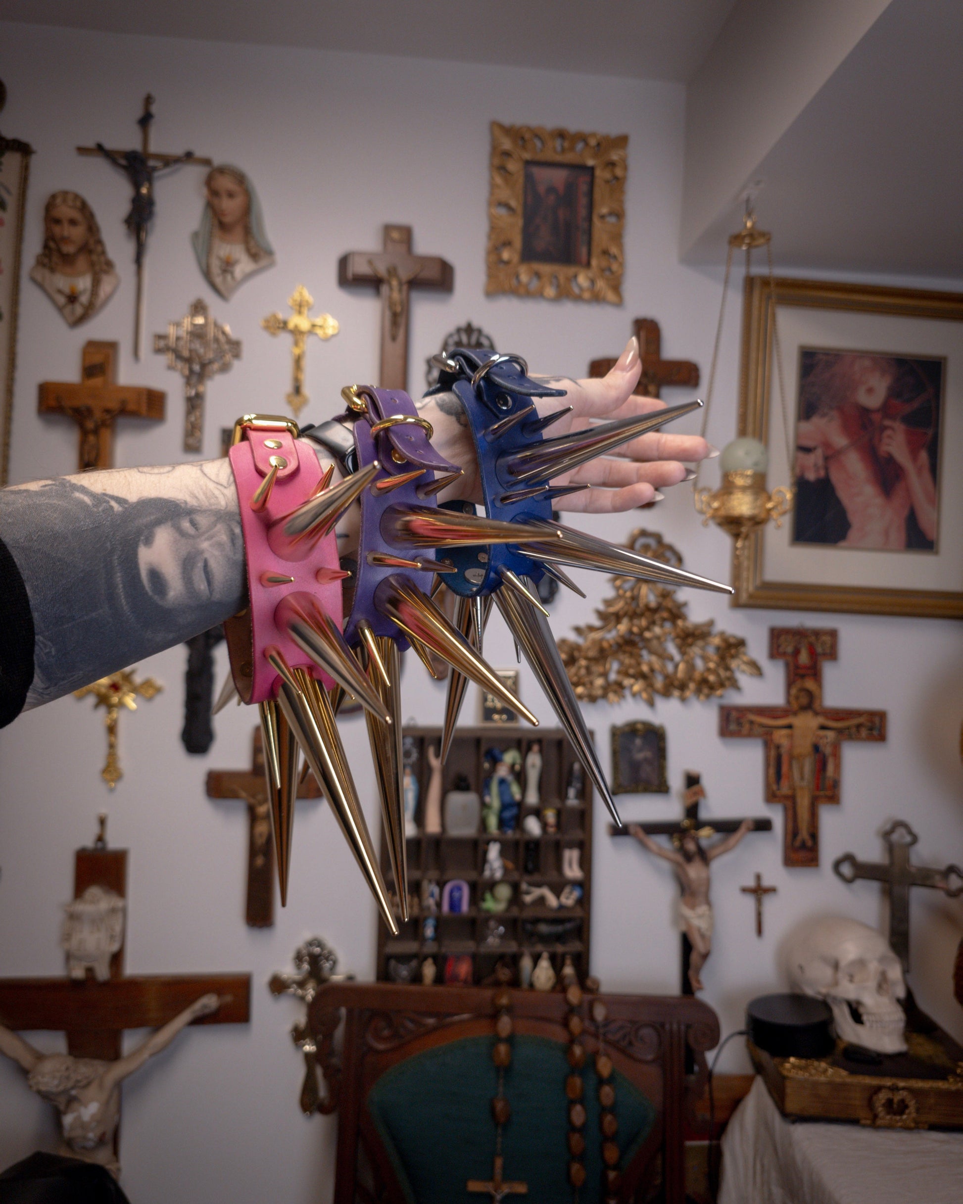 arm with large spiked collars hanging from, against a wall with gothic and religious decor