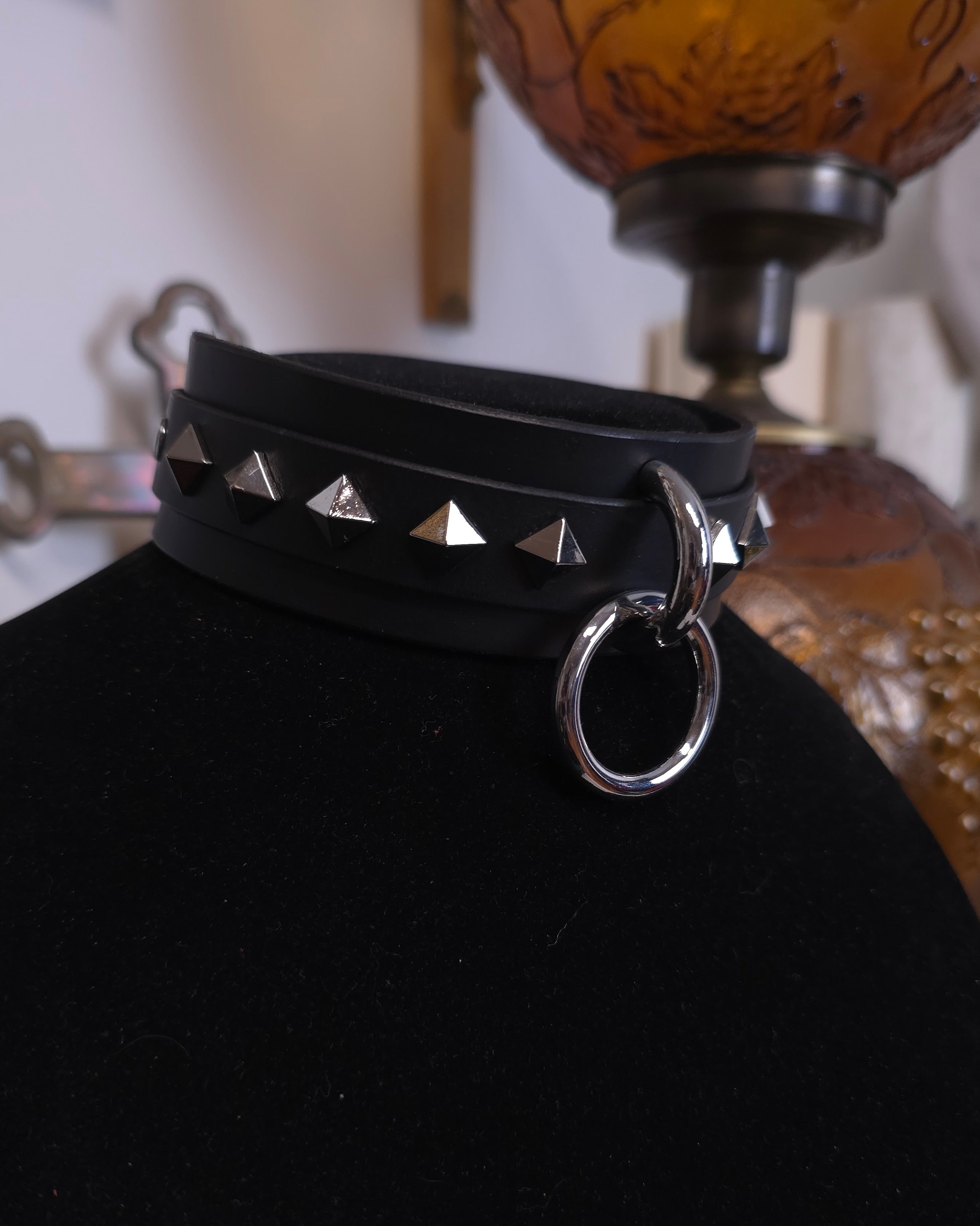 Black leather choker with silver studs and ring on a black stand.