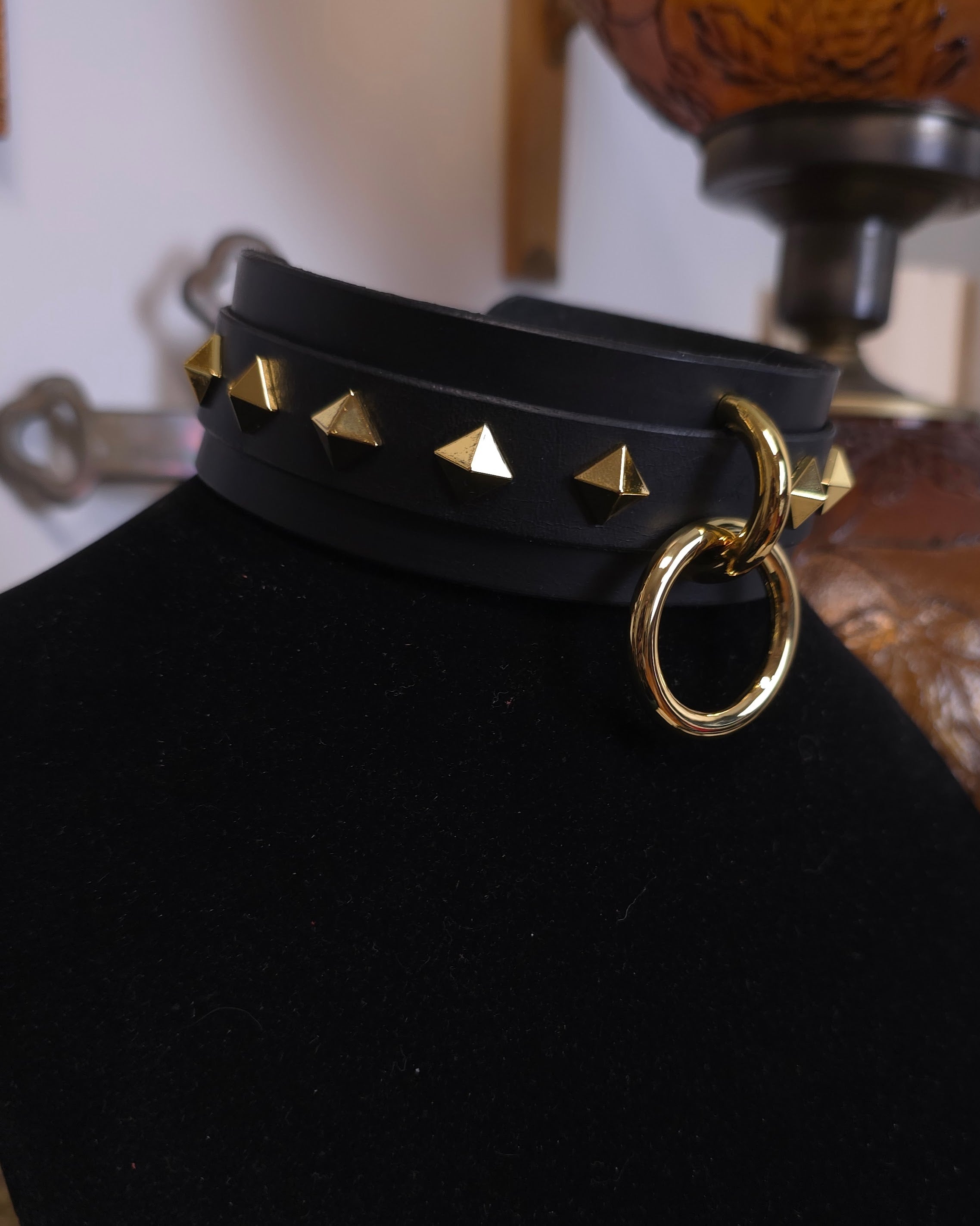 Black choker with gold studs and ring on a black stand.