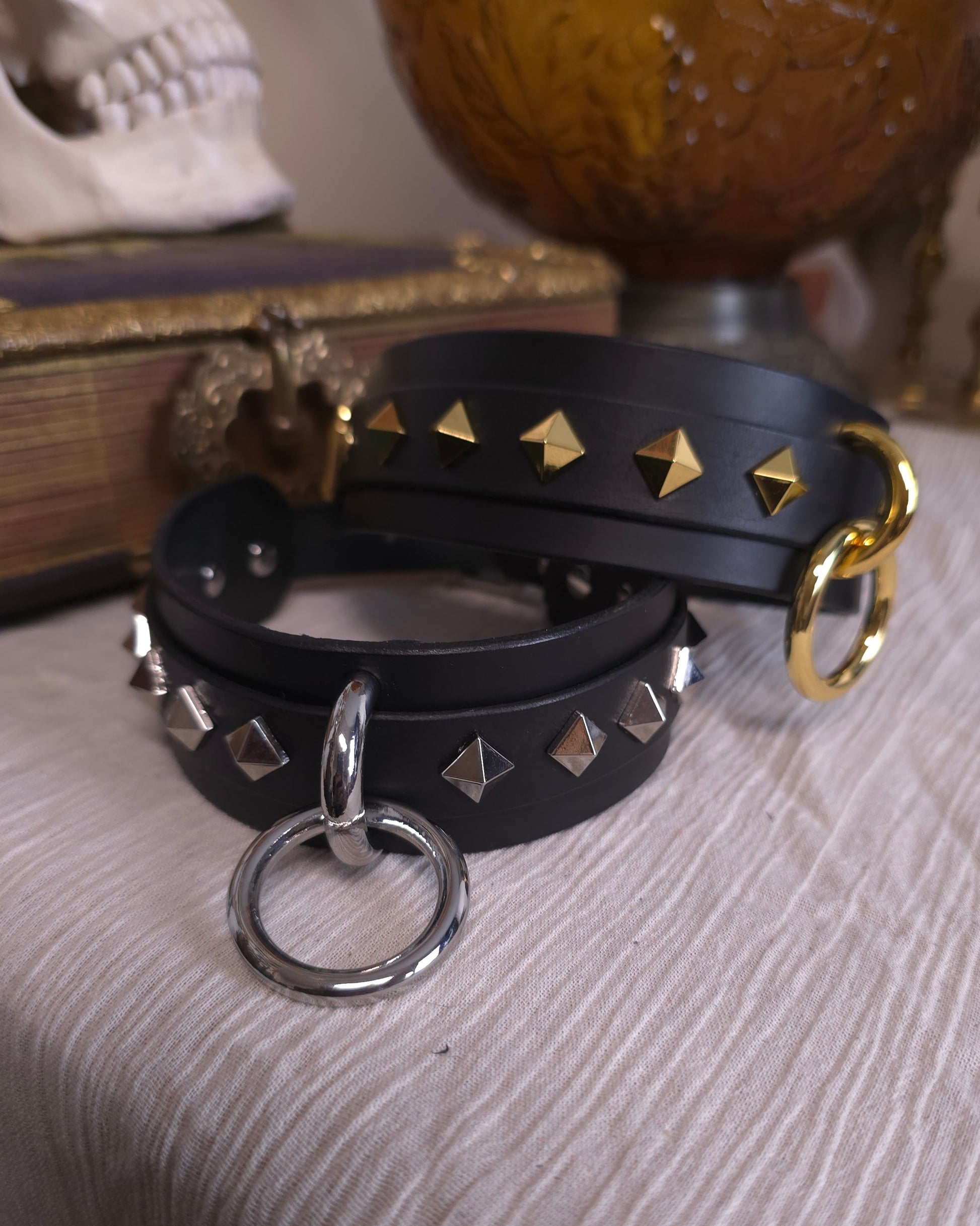 Black leather collar with gold and silver studs and rings on a textured surface.