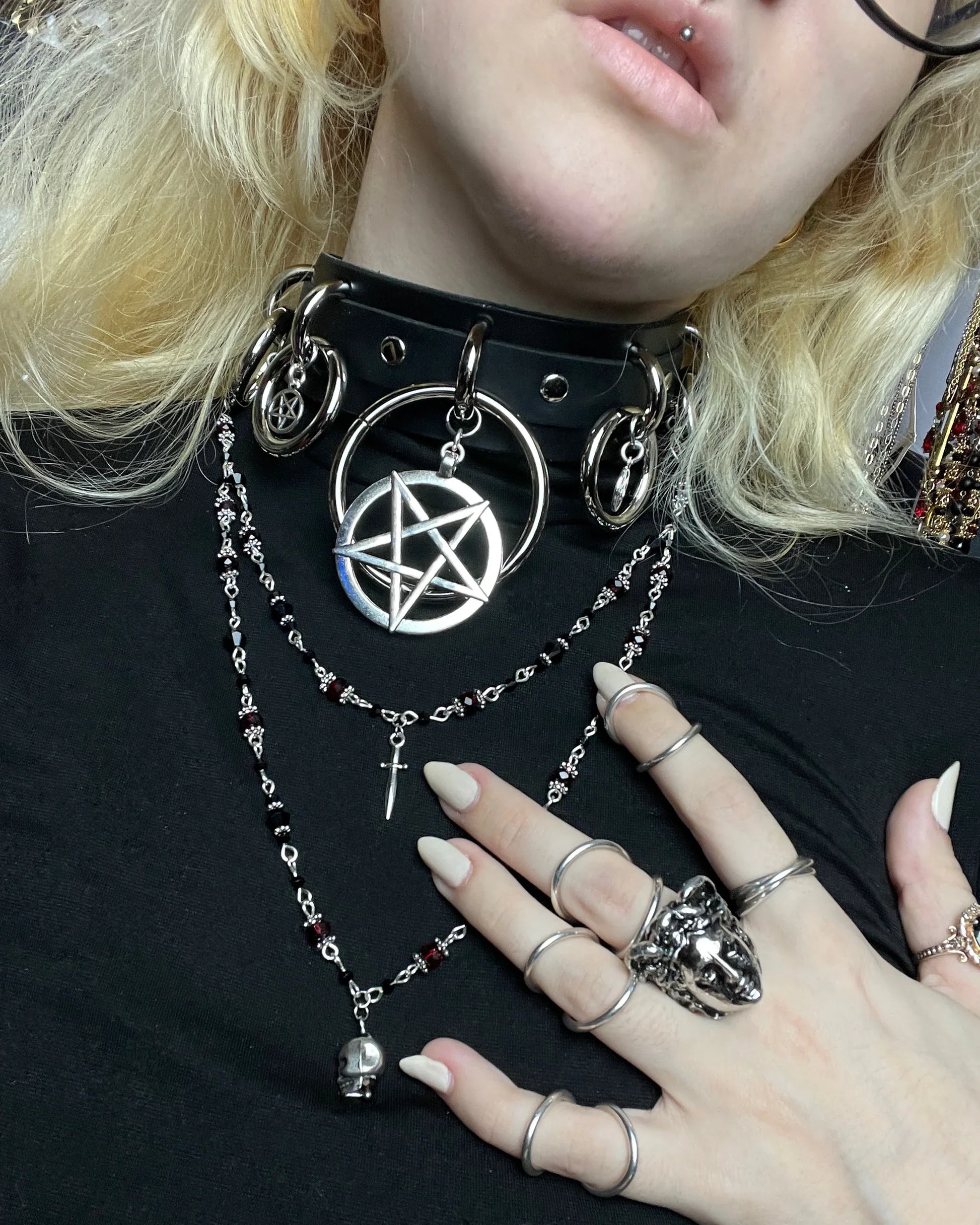 Person wearing a black choker with a silver pentagram pendant and multiple rings on fingers.