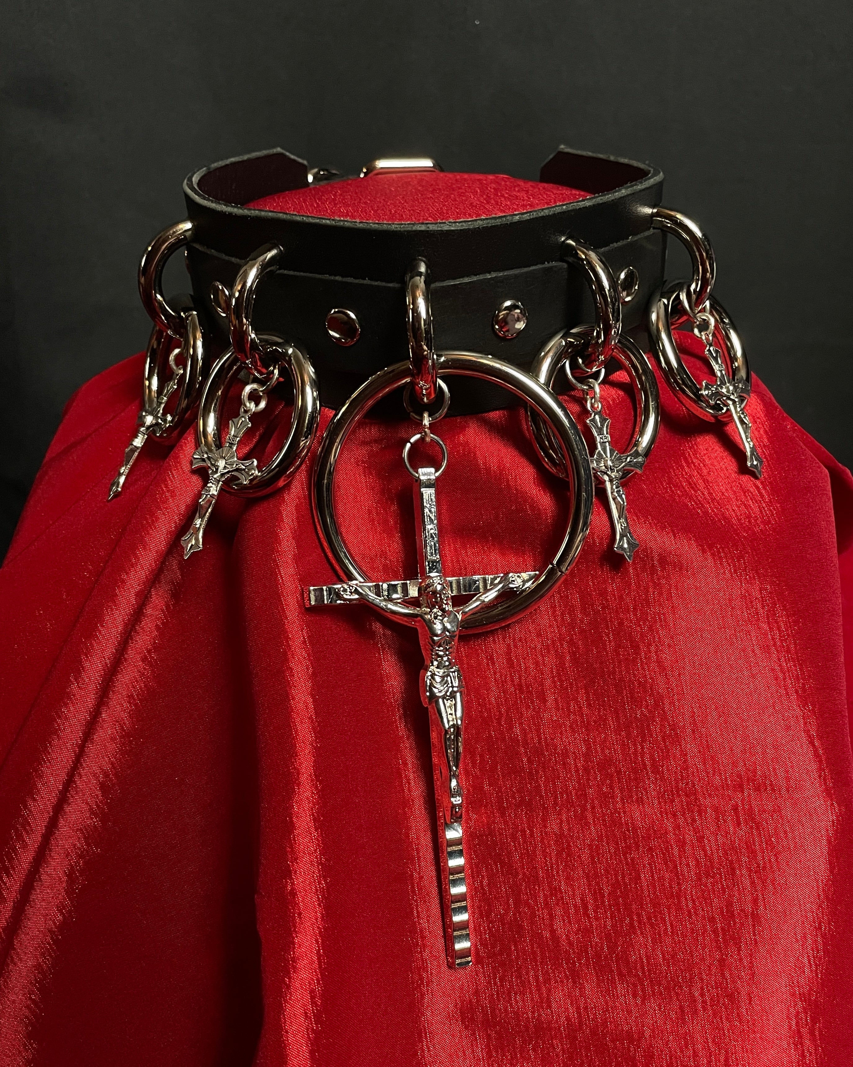 Black leather collar with metal rings and crosses on a red fabric background