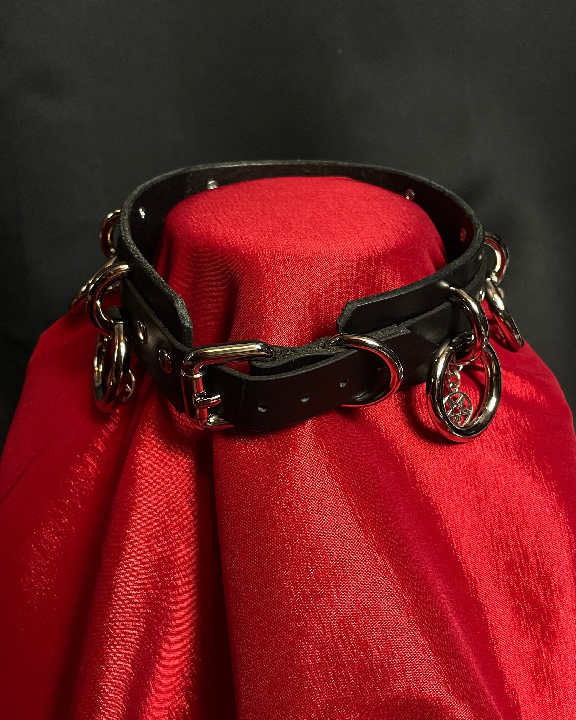 Black leather collar with metal rings on a red cushion against a dark background