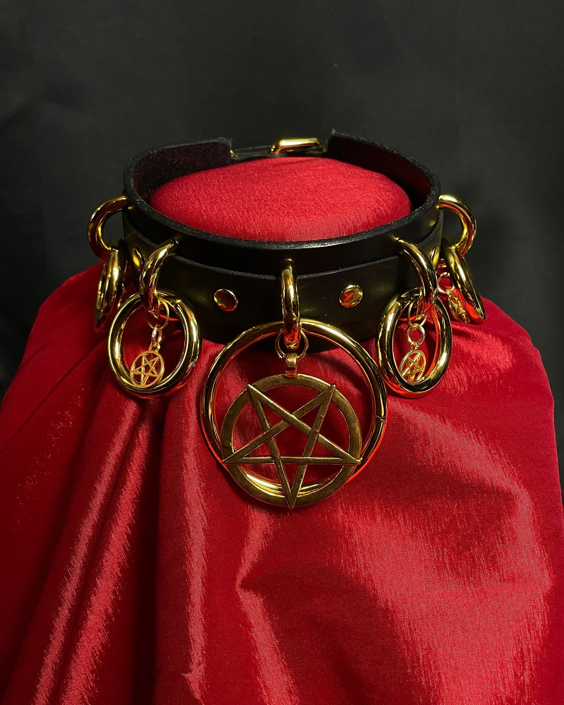 Black leather collar with gold hardware featuring a pentagram design on a red fabric background.