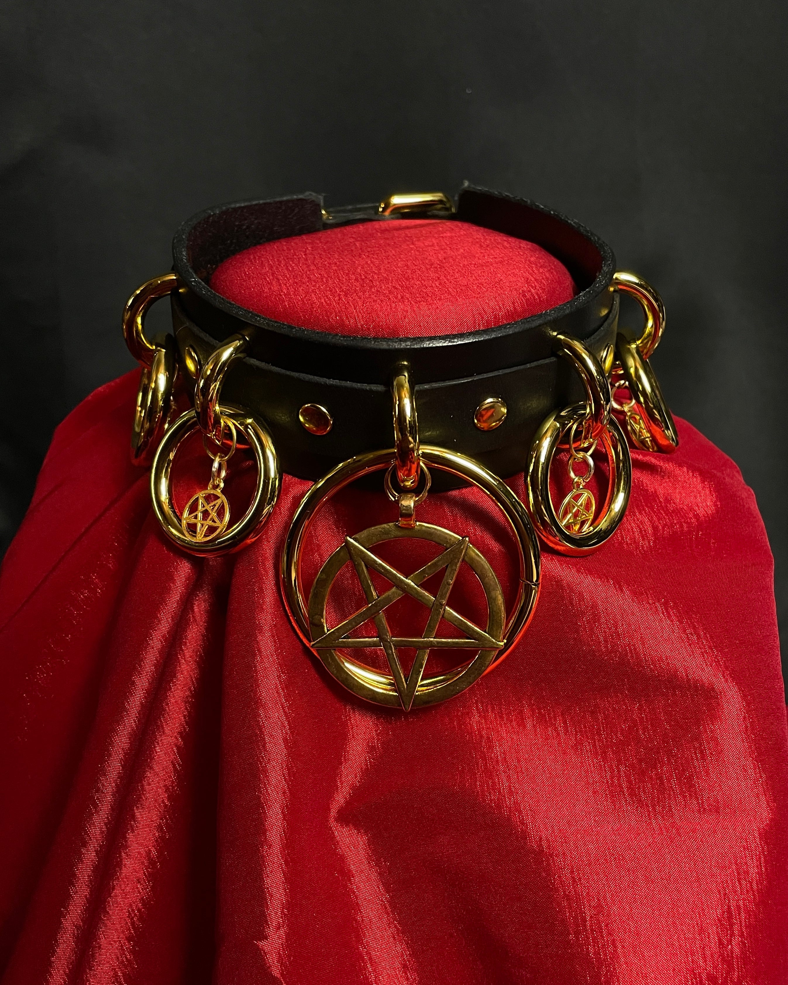 Black leather collar with gold hardware featuring a pentagram design on a red fabric background.