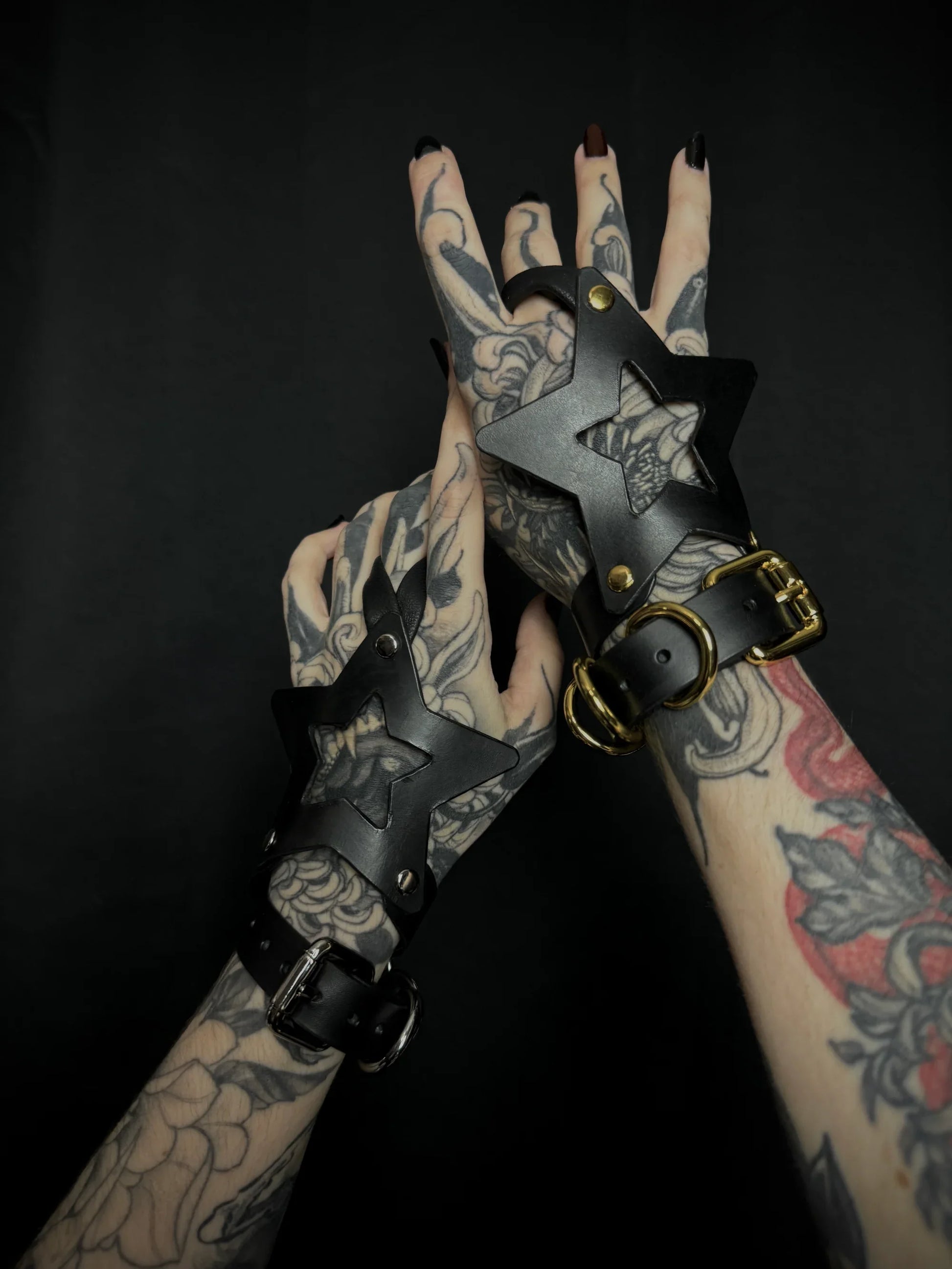 Tattooed hands wearing black leather gloves with star designs on a dark background