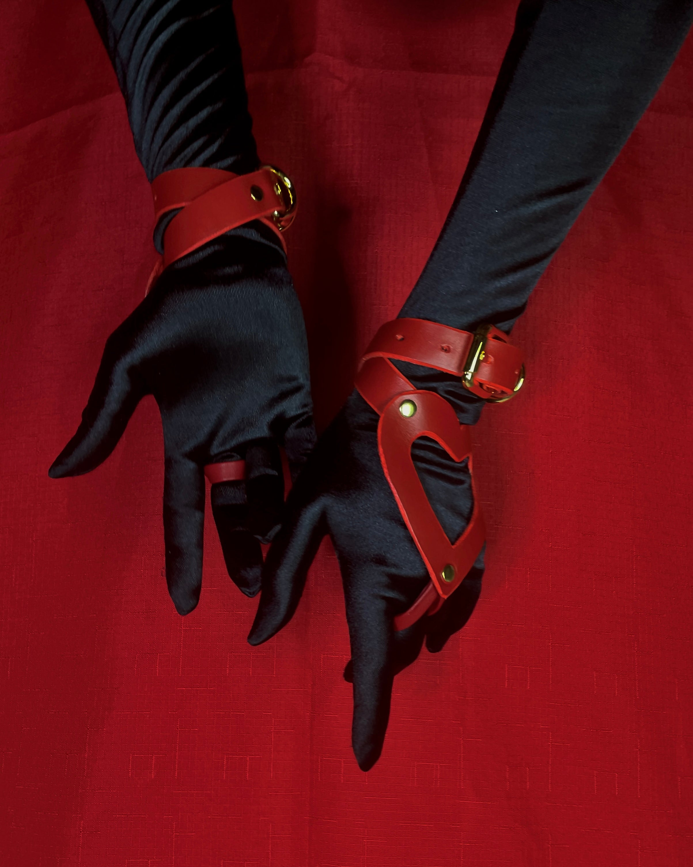 Black gloves with red leather straps on a red background