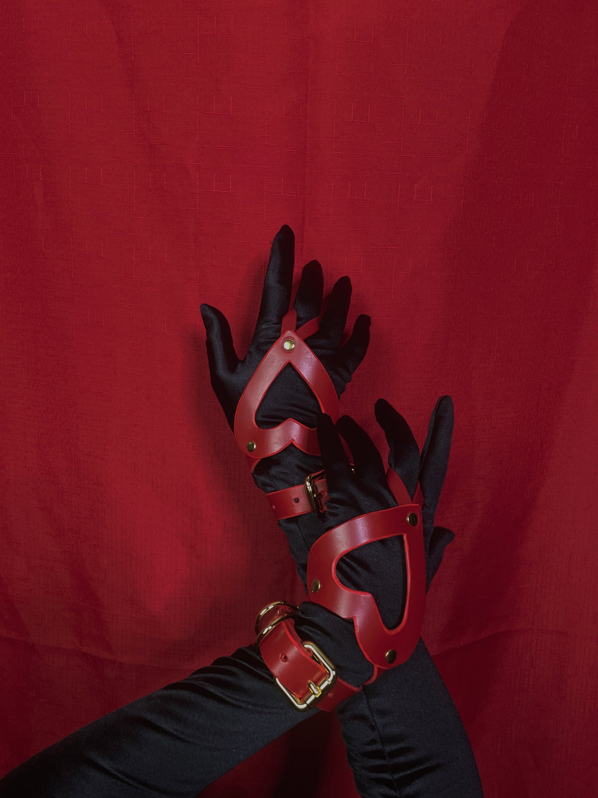 Red leather heart shaped gauntlets with gold accents on a red background 