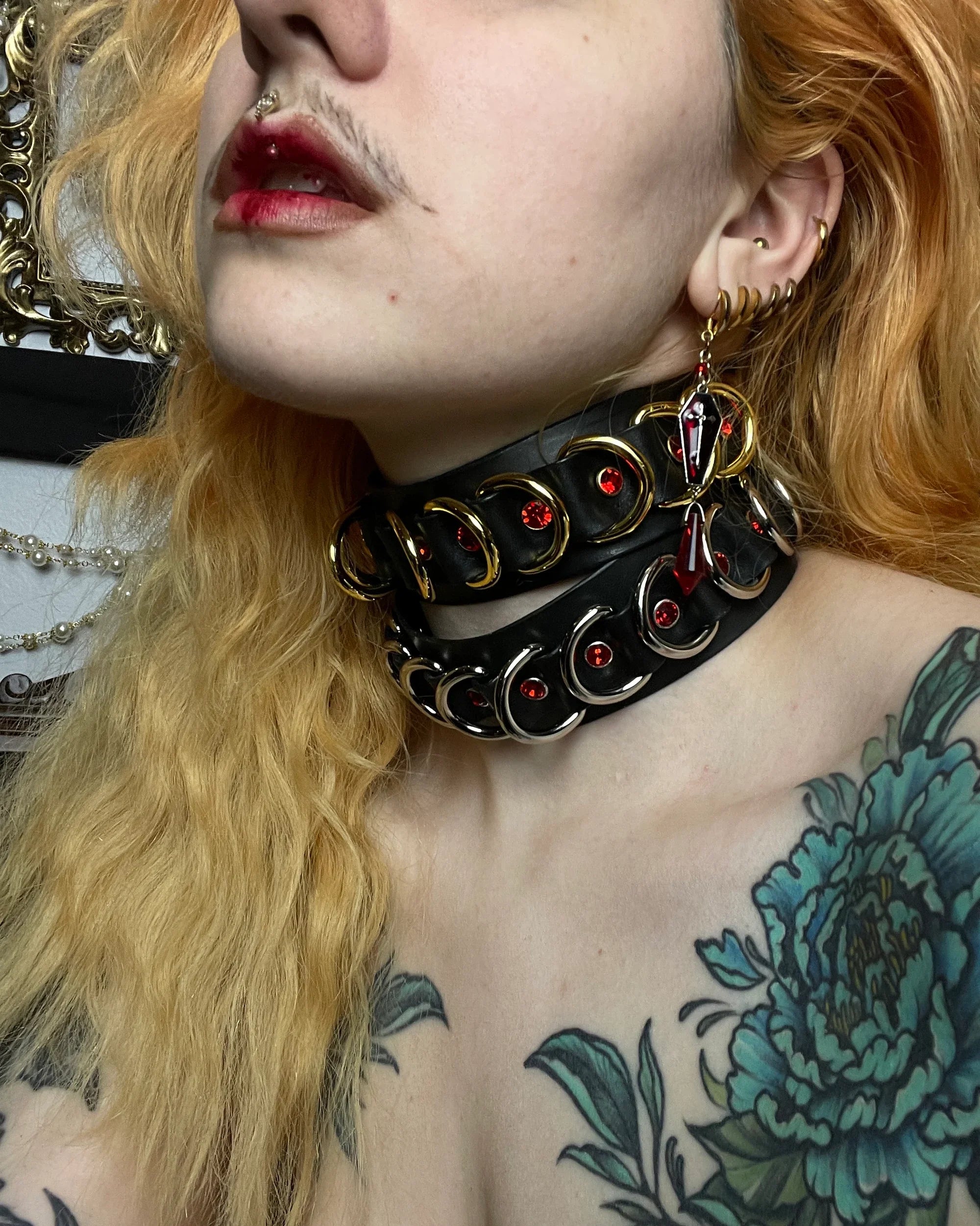 Person wearing two black leather choker with metal accents and red stones, close-up of neck and shoulder