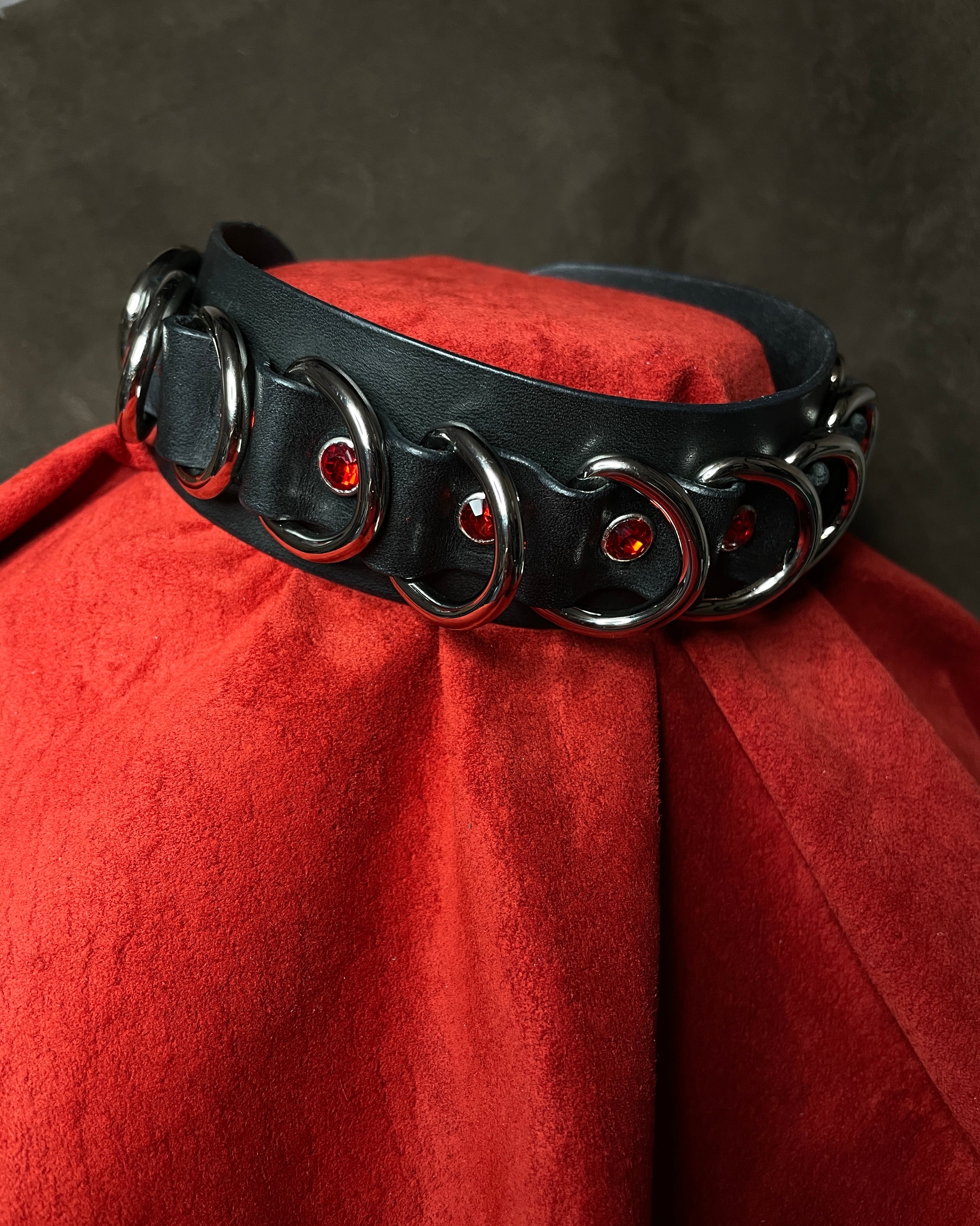 Black leather collar with red embellishments on a red fabric background