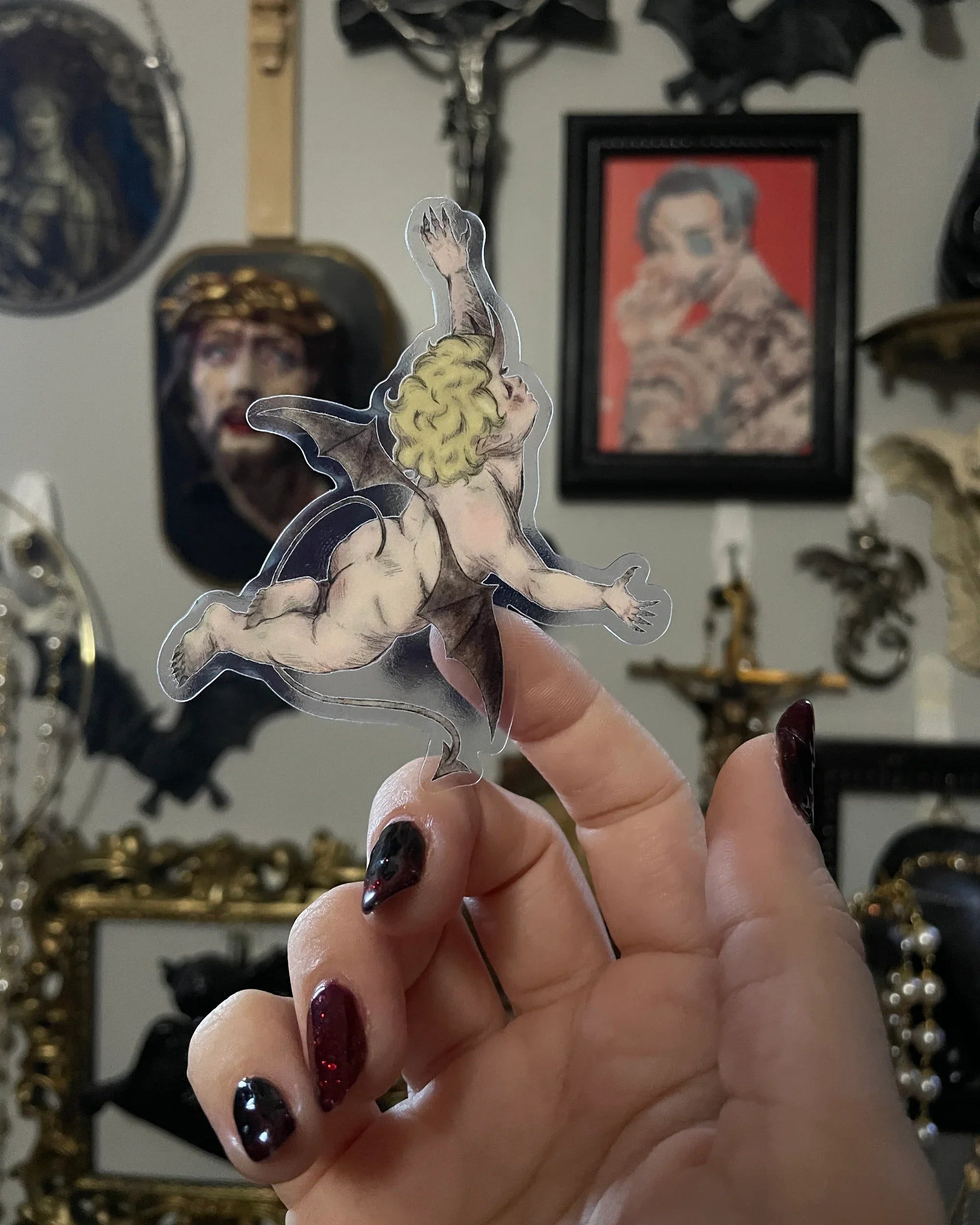 hand holding a transparent sticker with illustration of a demon cherub