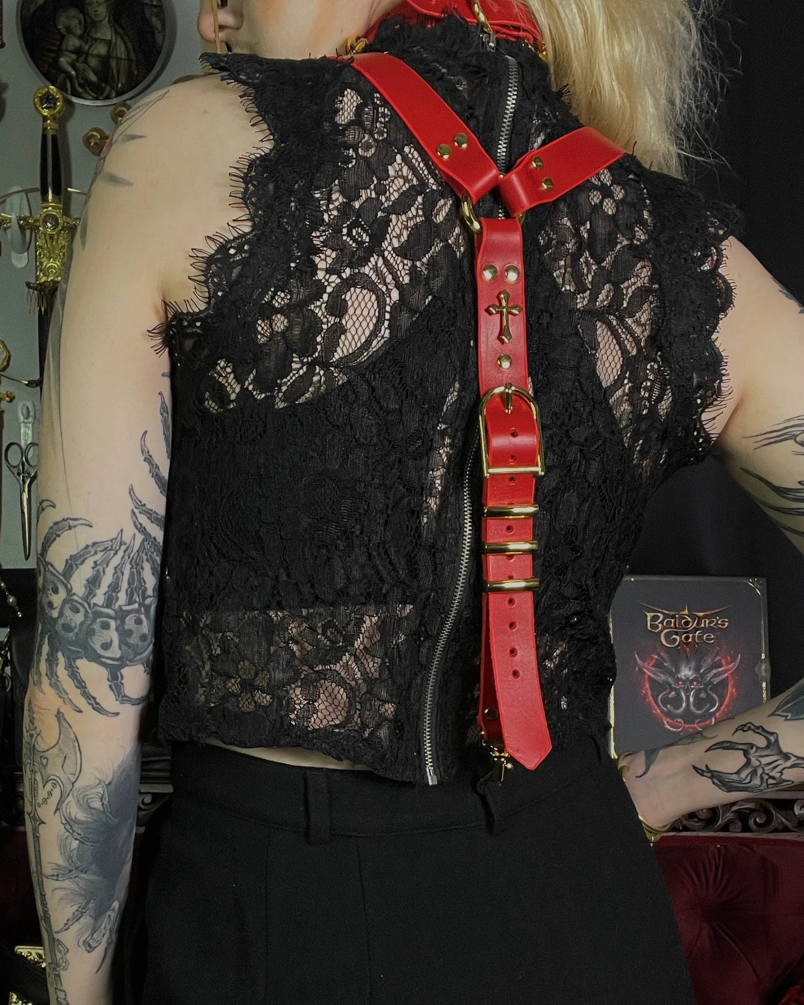 Person wearing a black lace vest with red suspenders over a dark background
