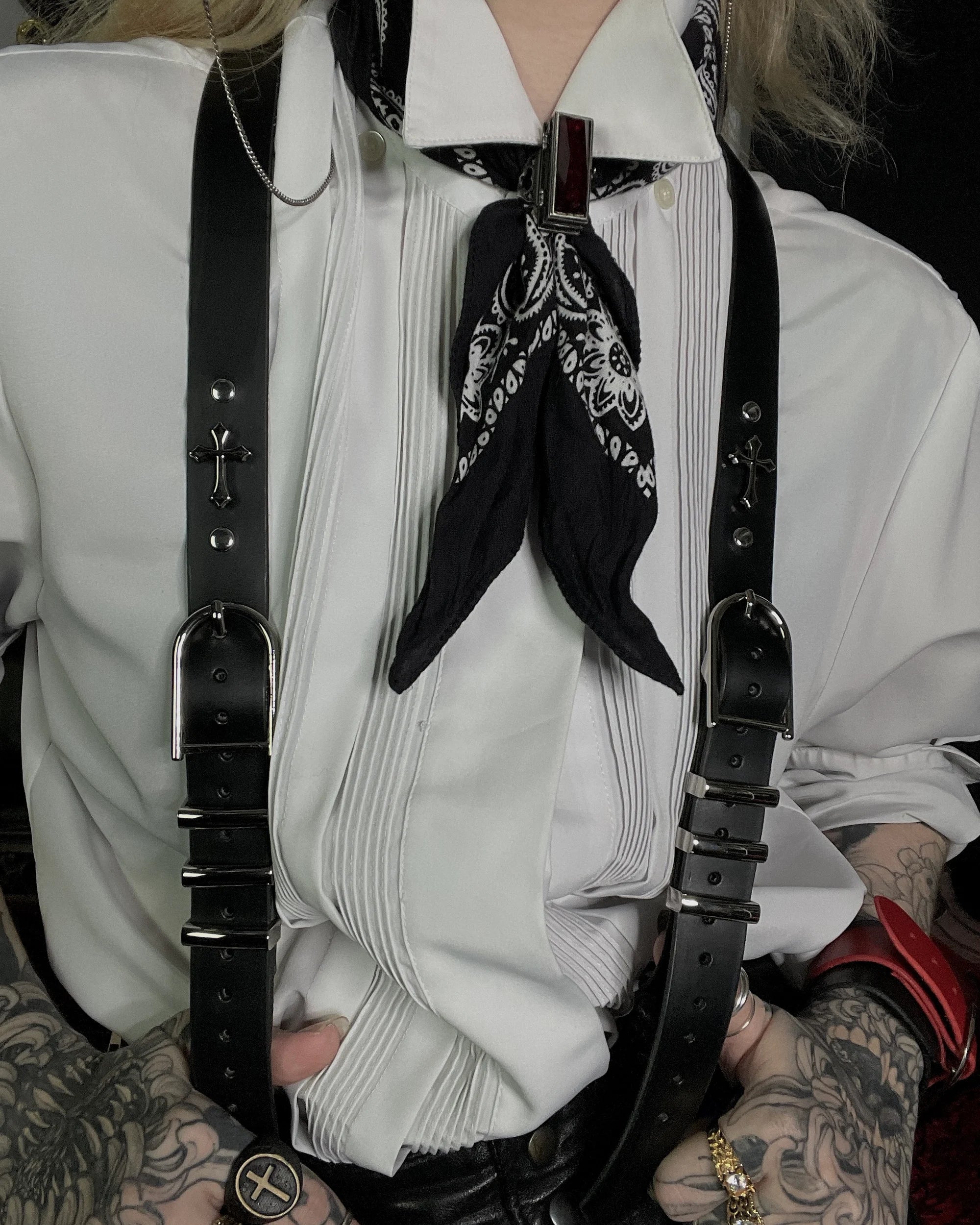 Person wearing a white shirt with black suspenders and a black bandana, with tattoos visible on arms.